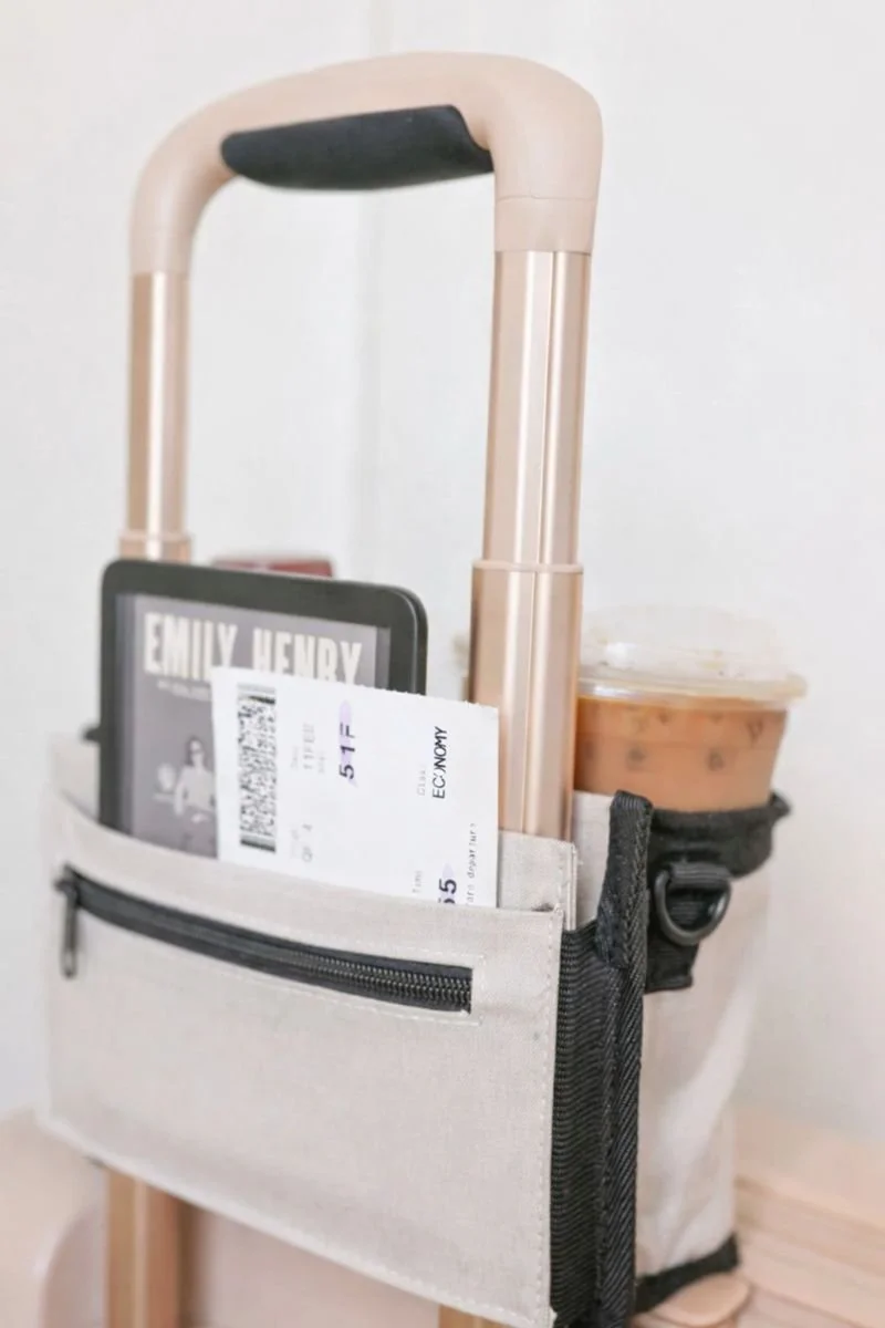 Samsonite beverage carrier that slides on to luggage displayed with drinks, a plane ticket, and kindle, showing it helps keeps travelers hands-free.