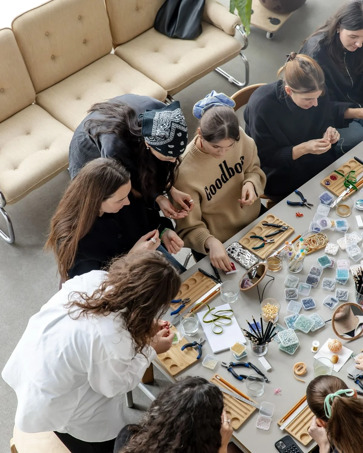 Group of people gathered around a table collaborating while making personalized charm and beaded jewelry with colorful supplies spread across the workspace, demonstrating participatory brand activation.