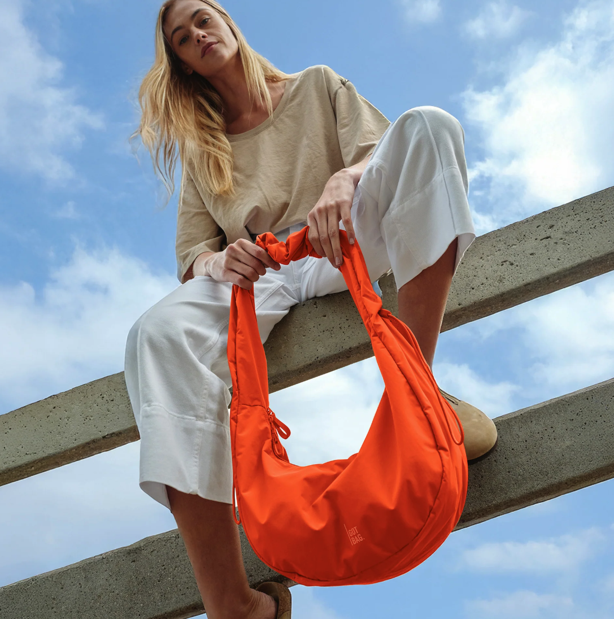 Photograph of model holding a vibrant orange crescent shaped bag from Got Bag, showcasing the trend towards primary colors.