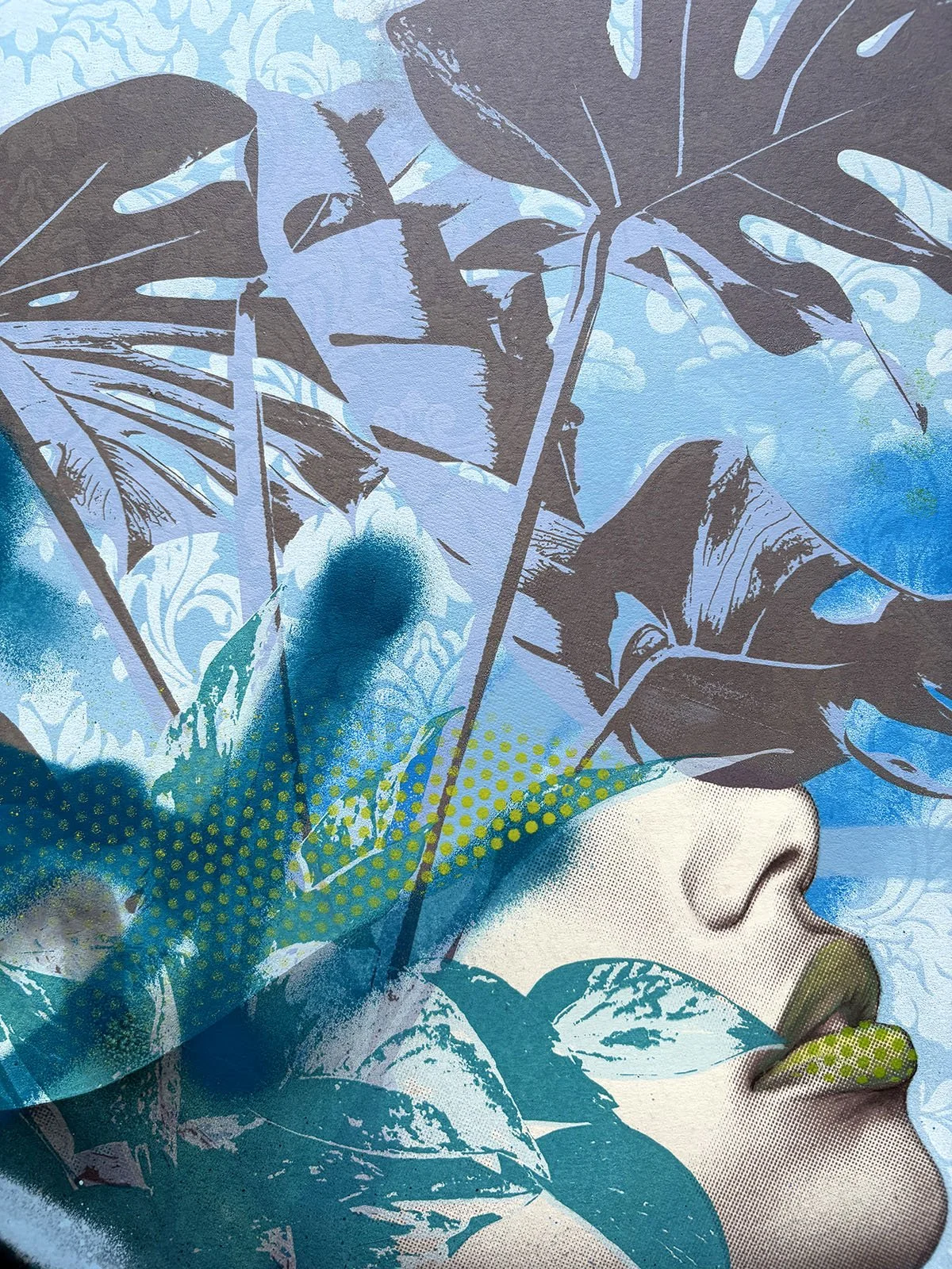 A mural painting depicting a woman's face with dark leaves covering her eyes and forehead, surrounded by blue and green abstract patterns and floral designs.