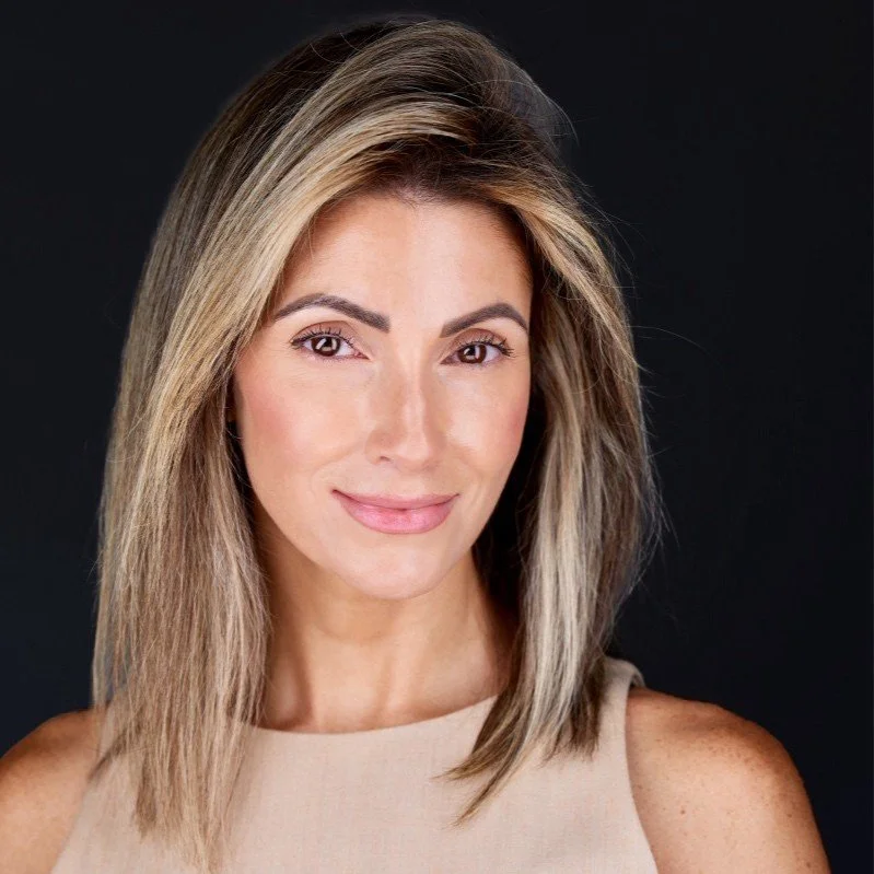 Portrait of a woman with shoulder-length blonde hair, wearing a beige sleeveless top, smiling against a black background.