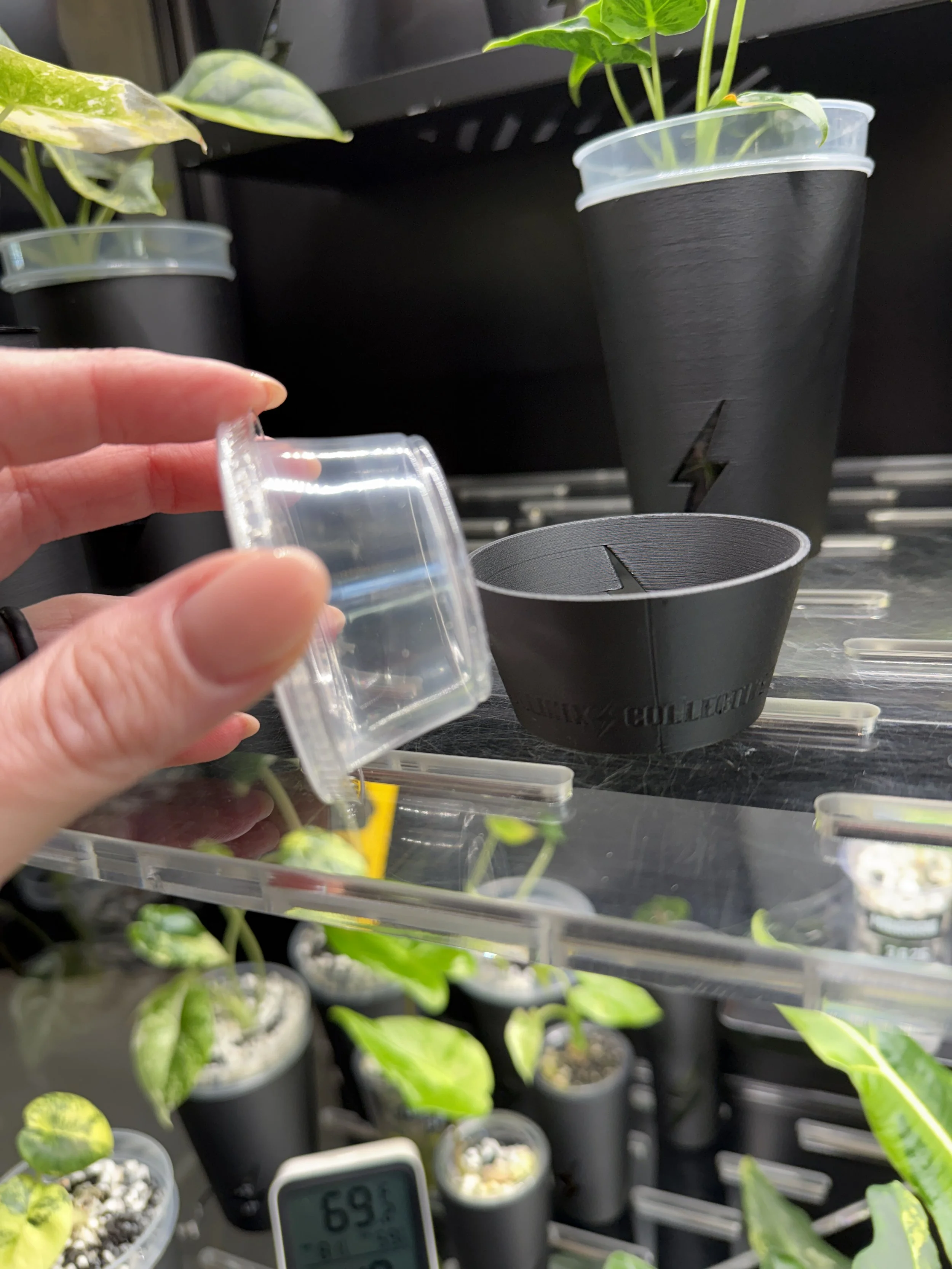 Hand holding clear 2oz condiment cup next to black 3D printed cover cup showing size and fit comparison