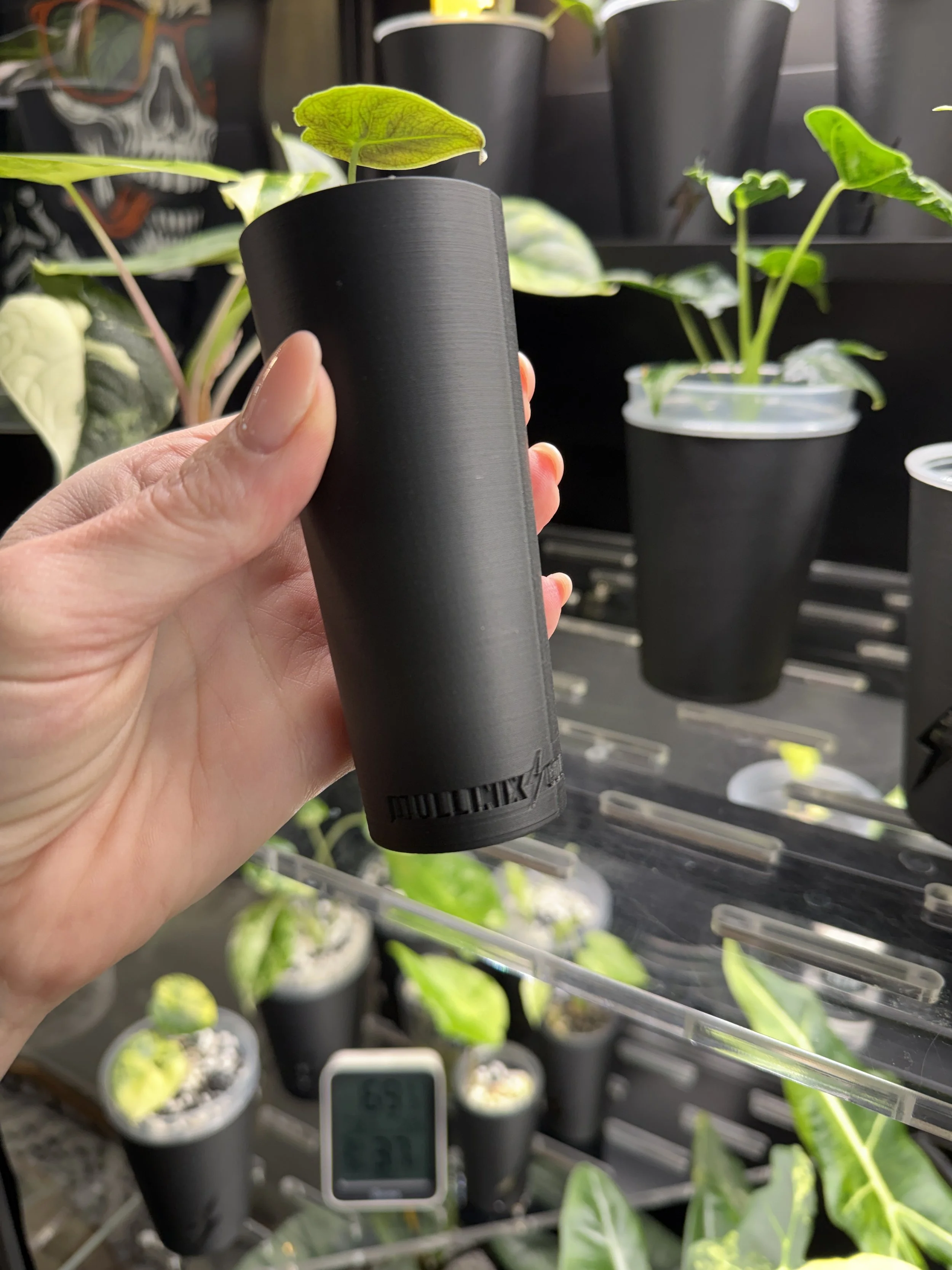 Hand holding matte black corm cup cover showing smooth finish and Mullinix Collective branding on bottom.