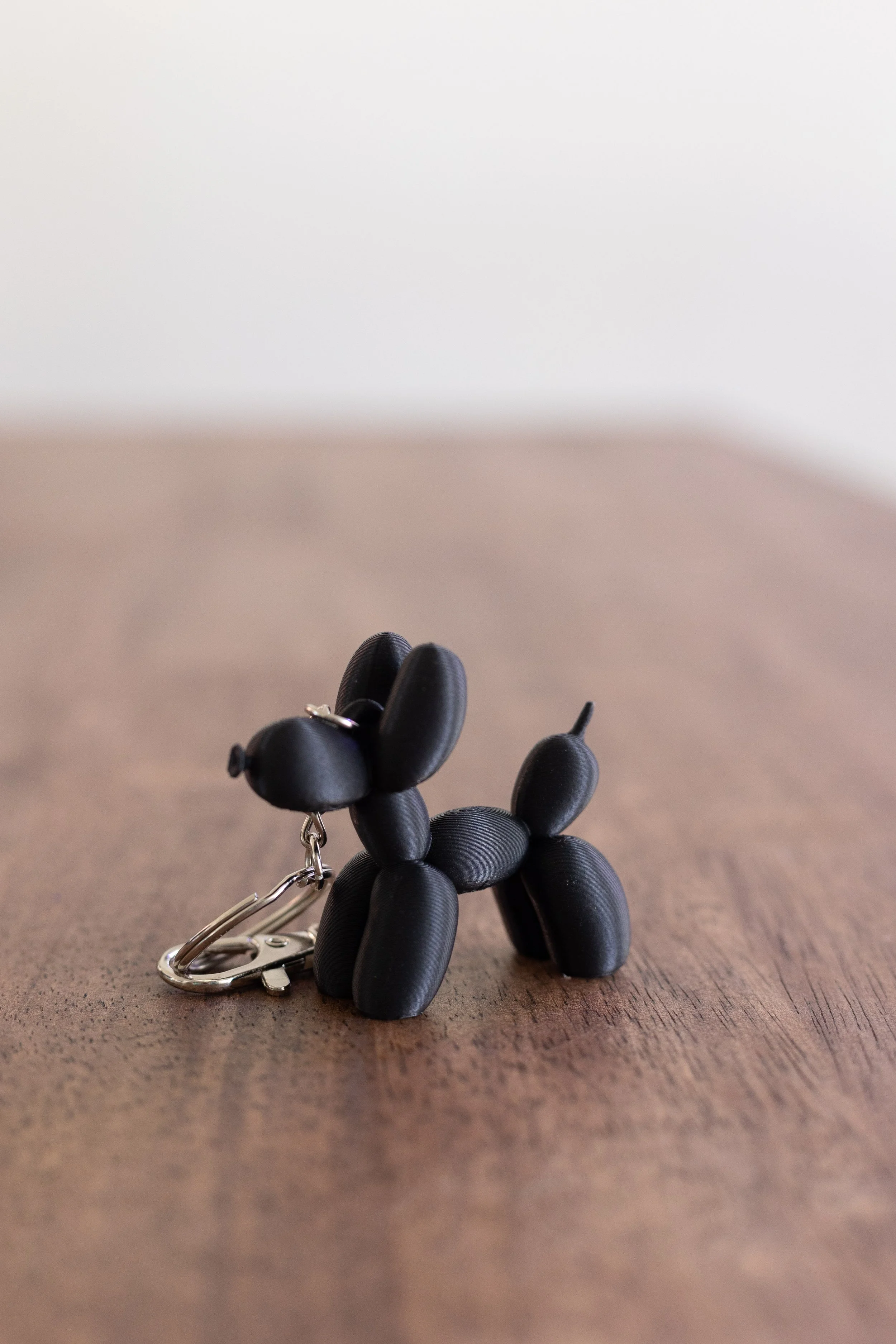 Black and purple gradient colored balloon dog keychain displayed on a wooden surface with simple background.