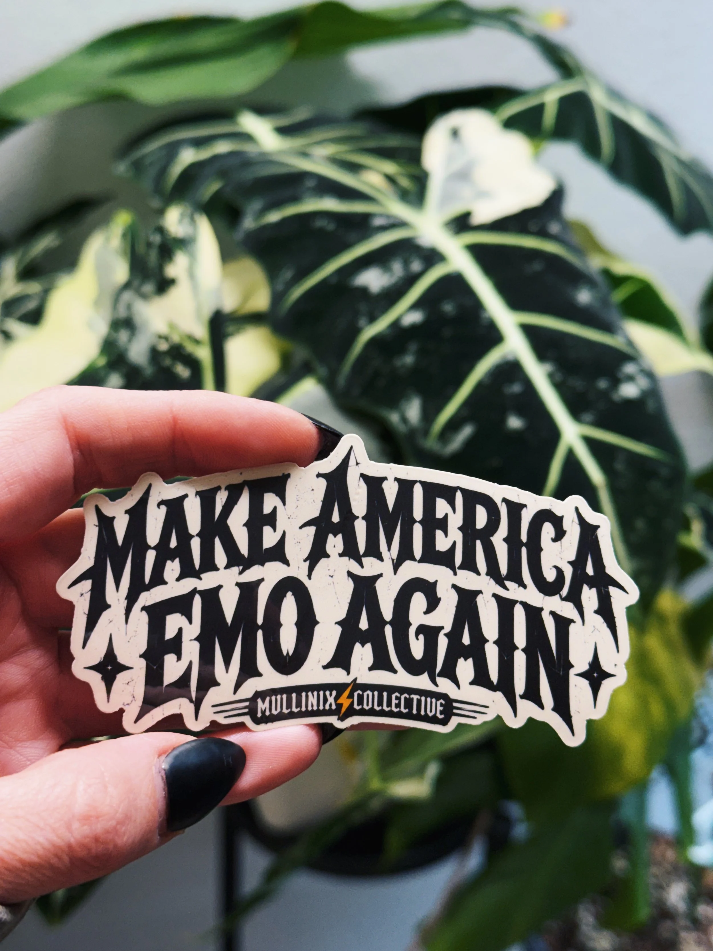 4 inch Make America Emo Again vinyl sticker with black distressed lettering and Mullinix Collective logo held in front of houseplants