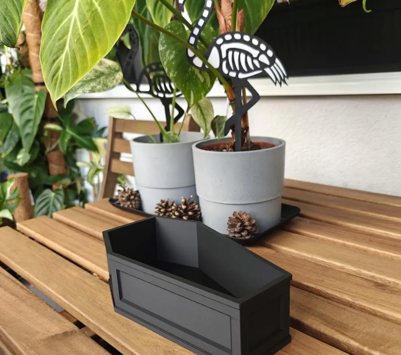 Empty coffin-shaped planter in matte black PLA with raised panel detailing, outdoor tabletop.