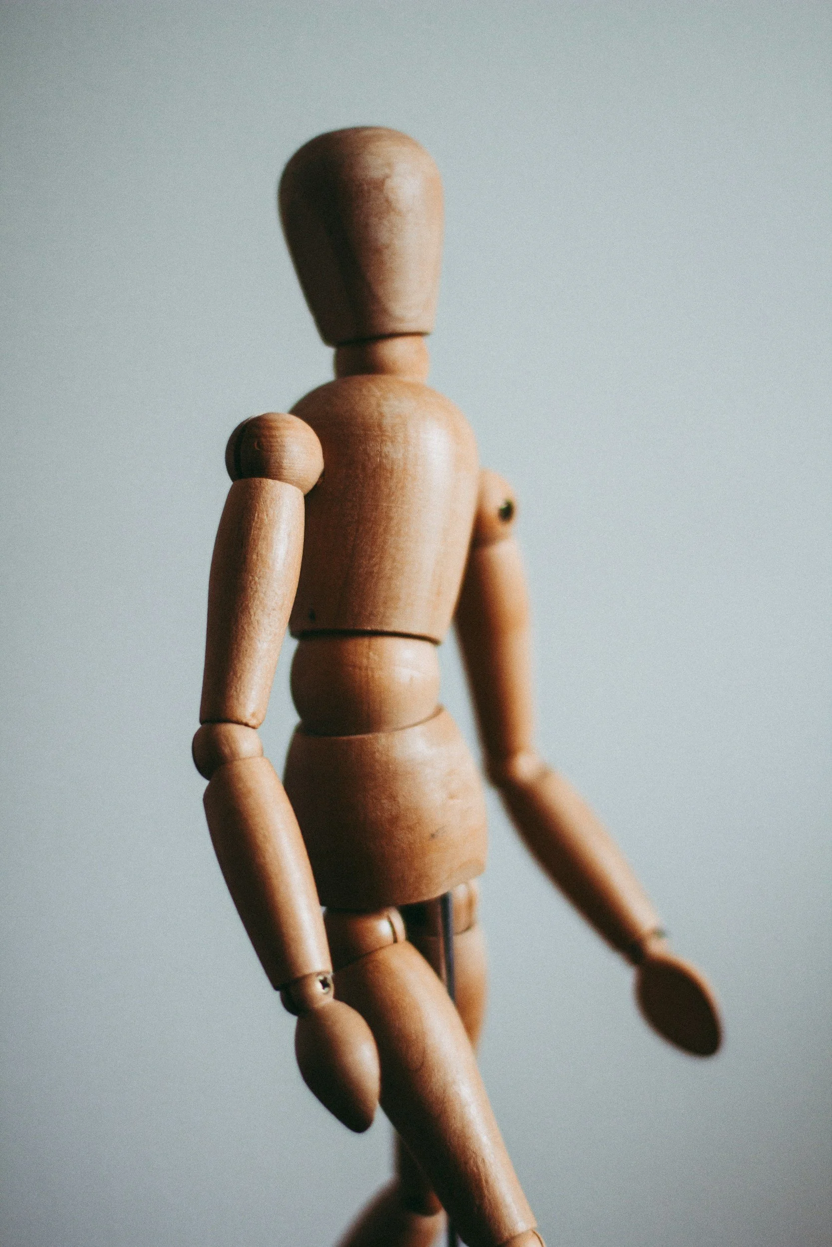 A close-up of a wooden mannequin doll standing against a plain background.