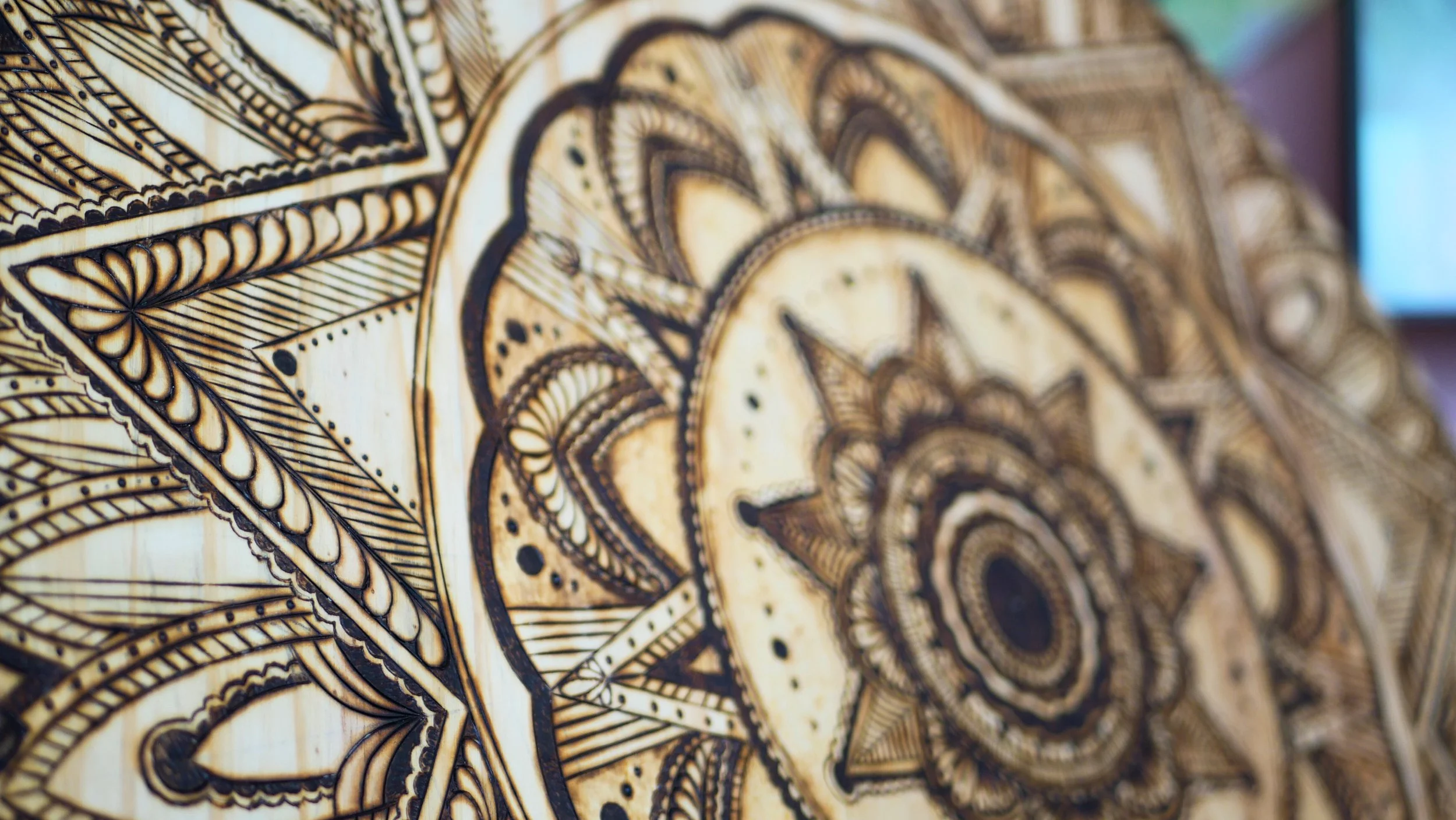 Close-up of a wooden panel with intricate black and brown geometric and floral patterns engraved in a mandala style.