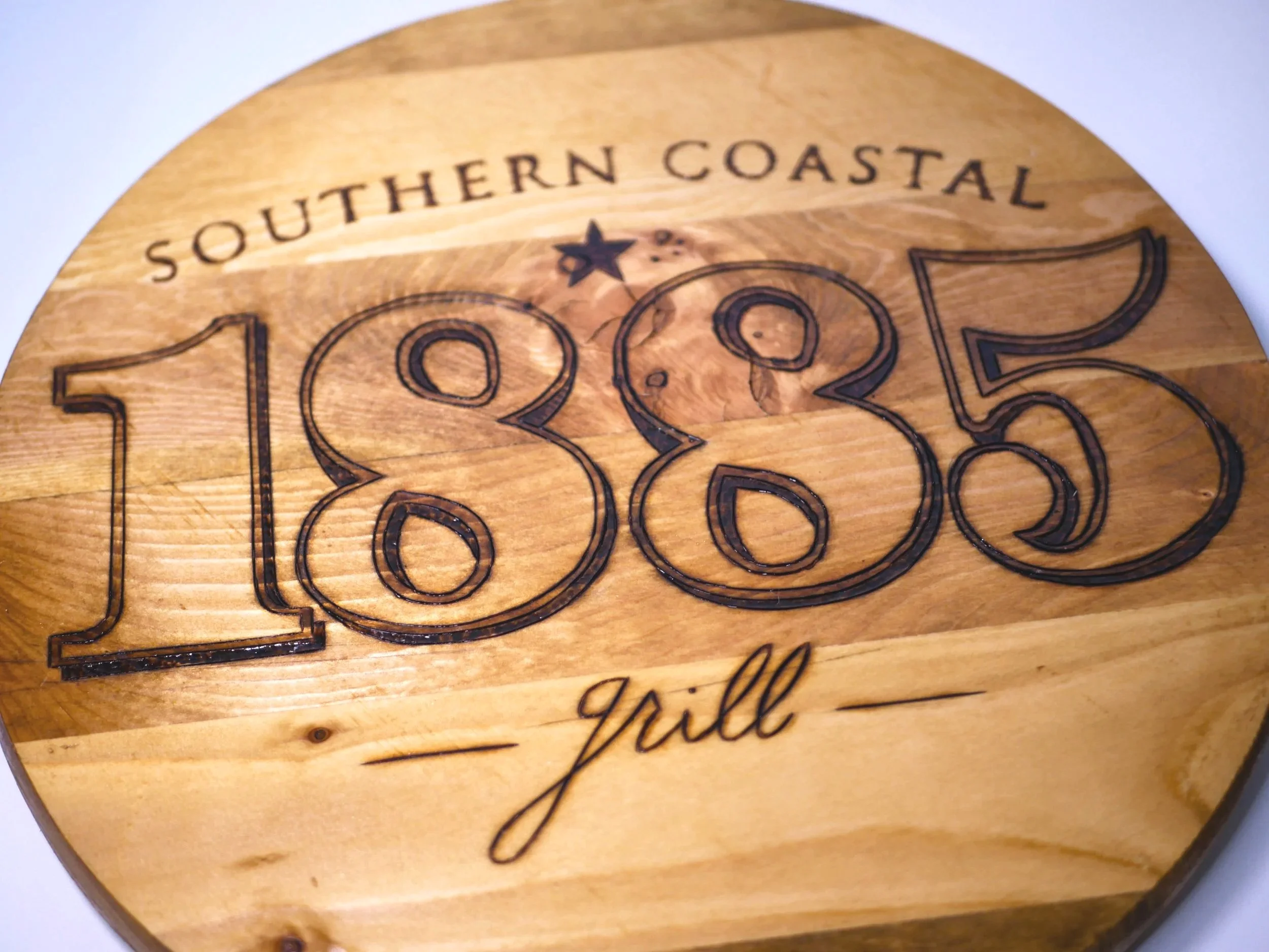 Wooden sign with engraved text reading 'Southern Coastal 1885 Grill'.