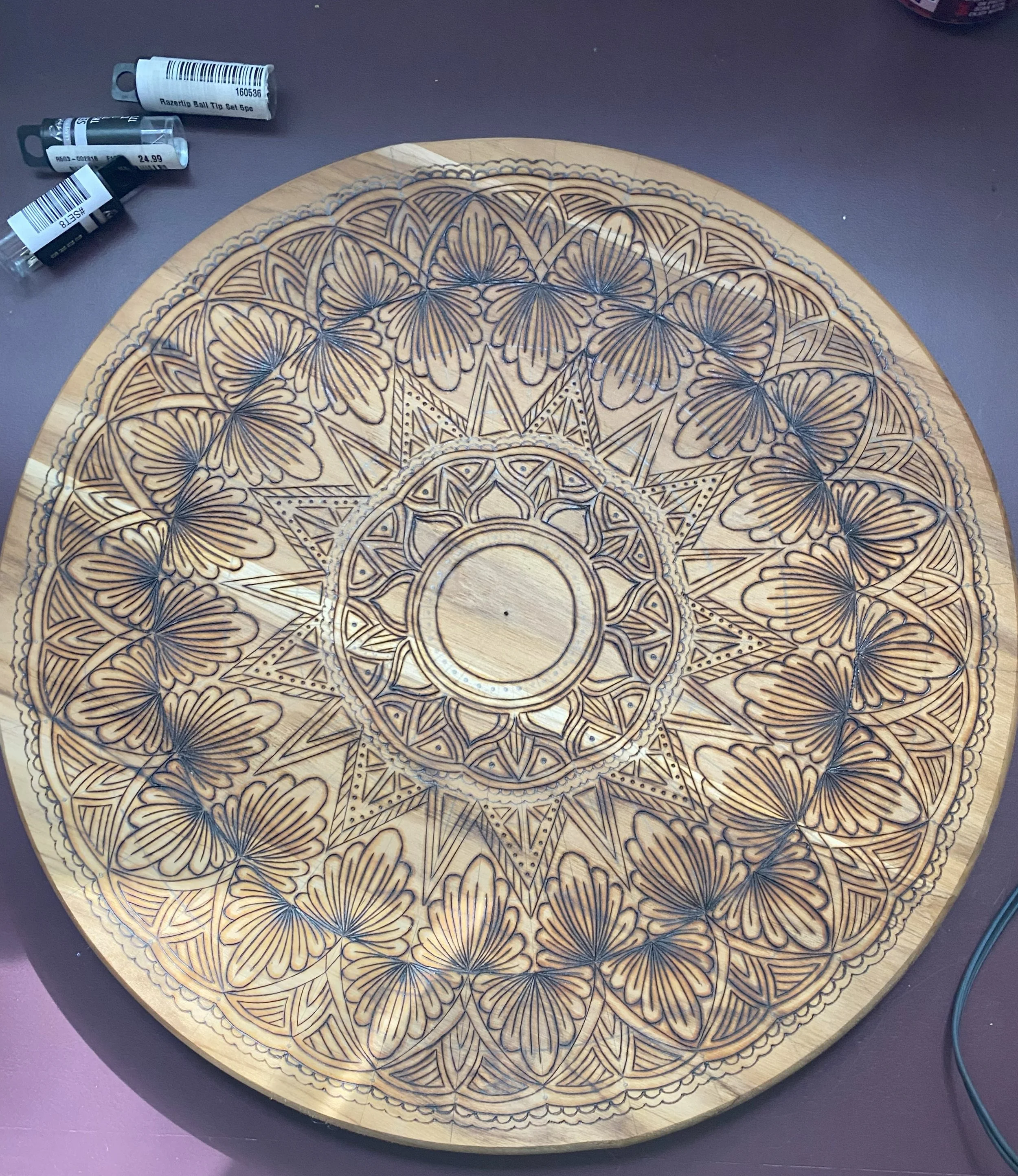 Wooden round panel with intricate carved pattern featuring butterflies and geometric designs.
