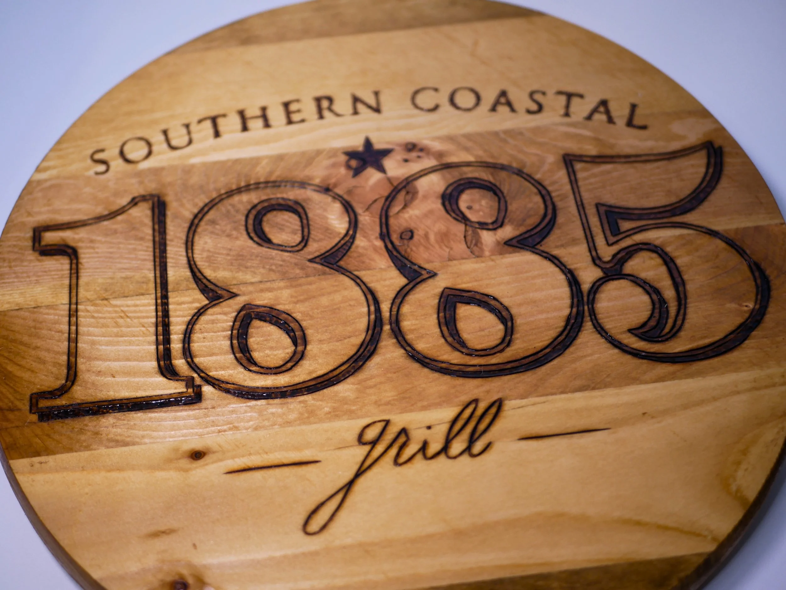 Wooden sign with engraved text reading 'Southern Coastal 1885 Grill'.