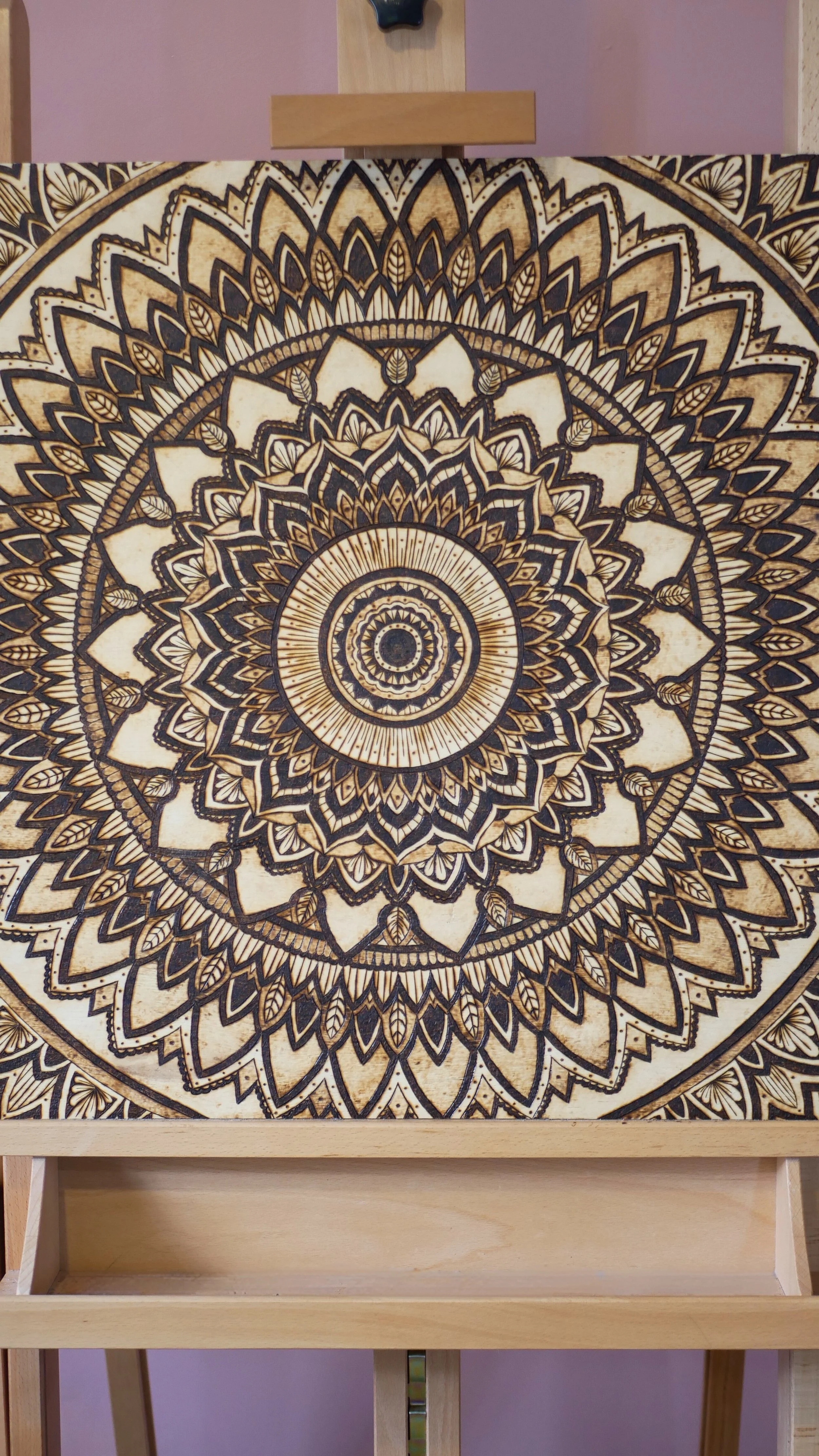 A wooden art piece with intricate black and tan mandala patterns, mounted on a stand.