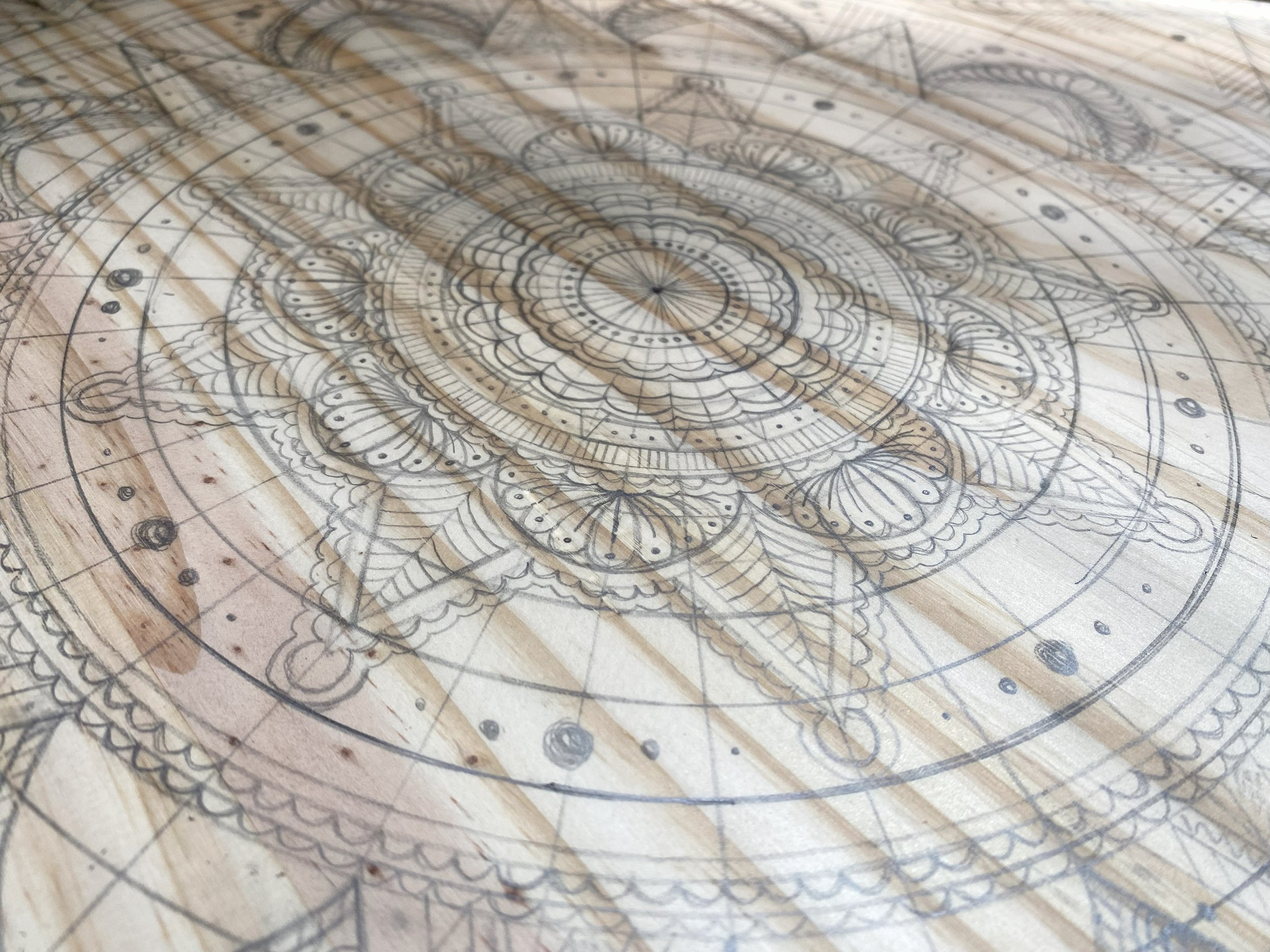 Close-up of an intricate geometric and mandala-style design sketched on wood, with detailed patterns and circular elements.
