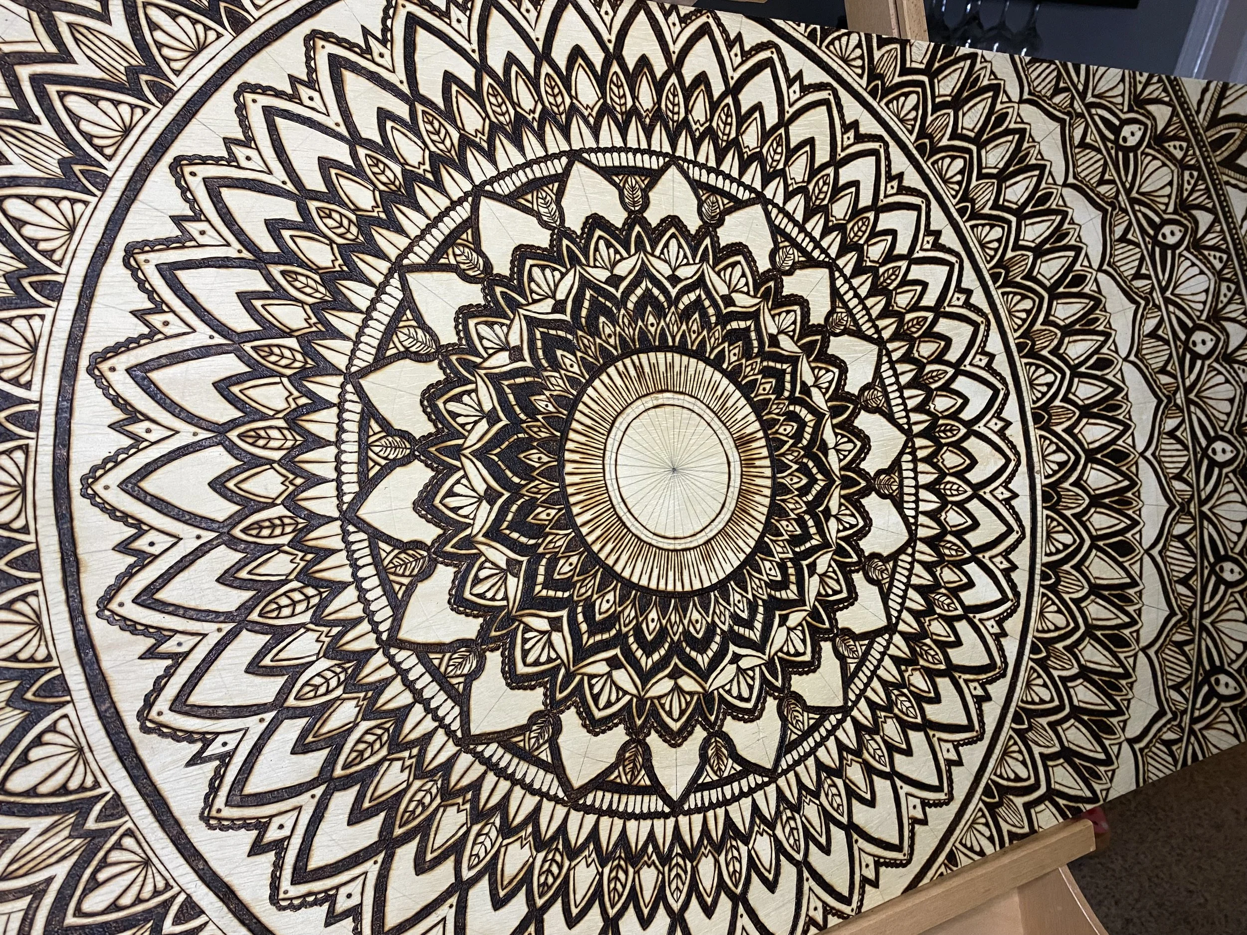 A detailed mandala design on a wooden surface with intricate geometric patterns in black and natural wood colors.
