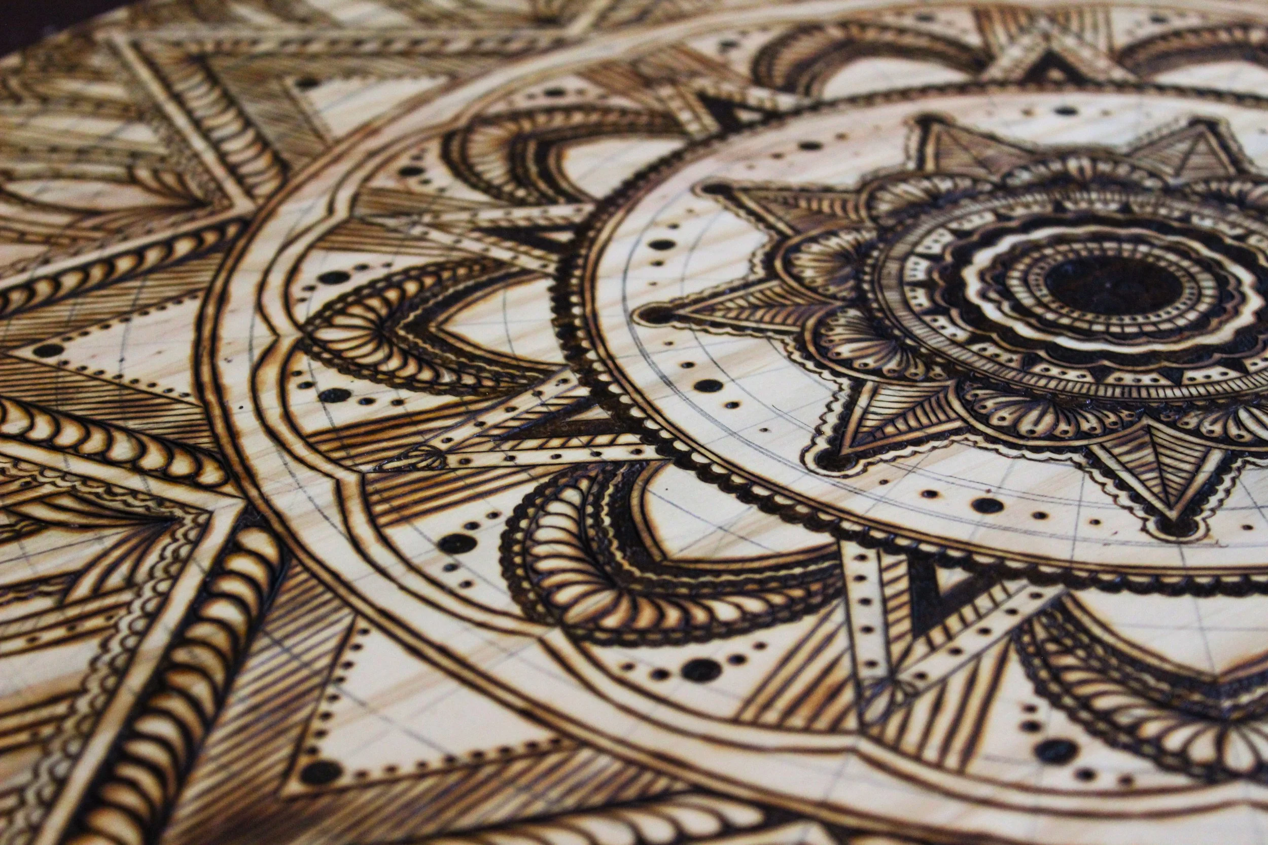 Close-up of an intricate, geometric wooden mandala design burned or etched into a surface.