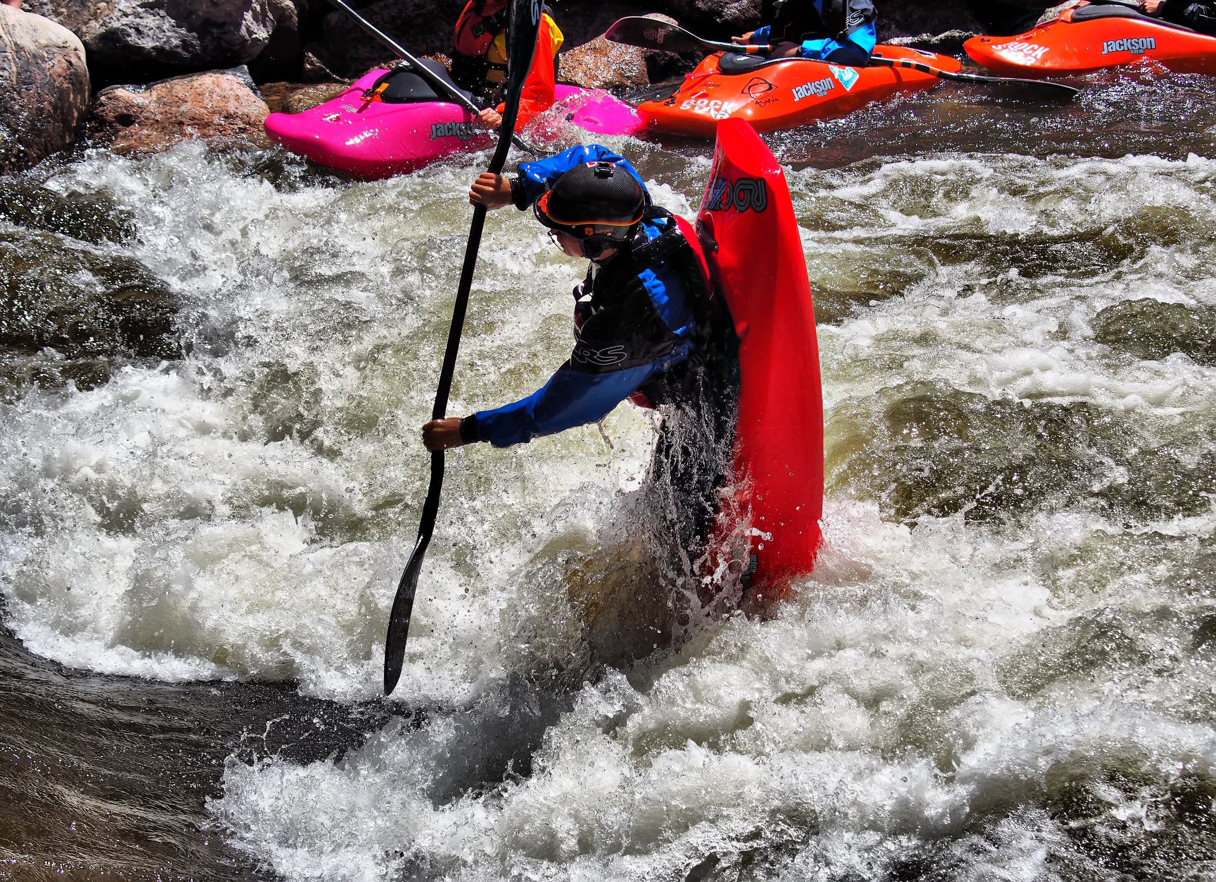 People kayaking on a river with rocks and white water.