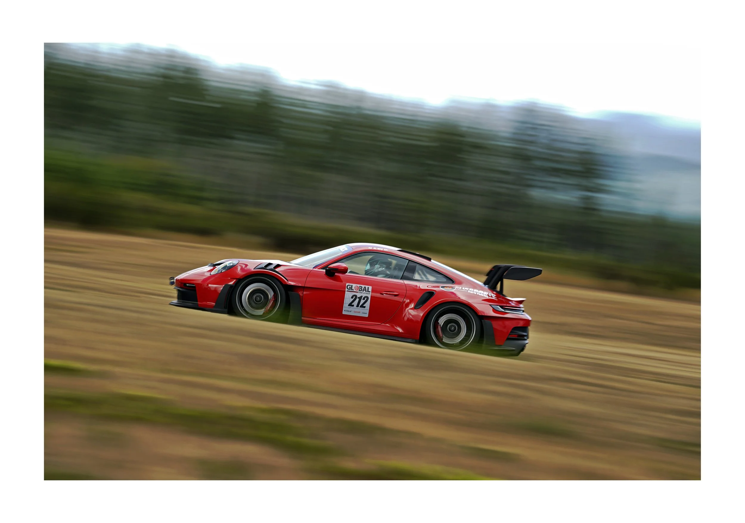 A red race car speeding on a track with a blur of green trees and sky in the background.