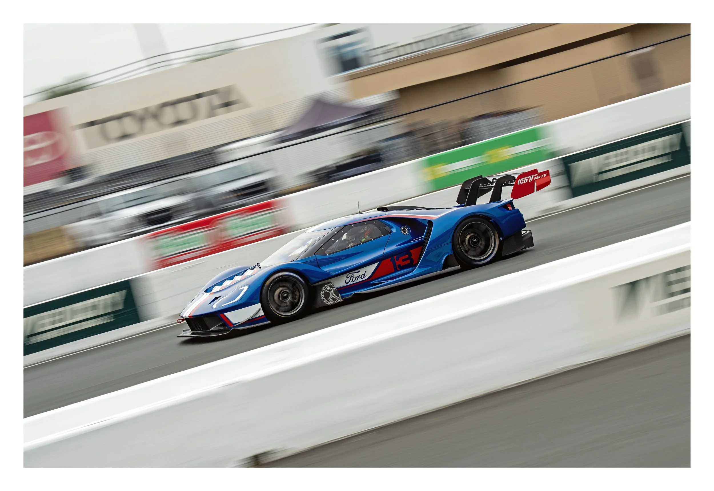 A blue race car with Ford branding and a red rear wing, speeding on a race track with a blurred background.