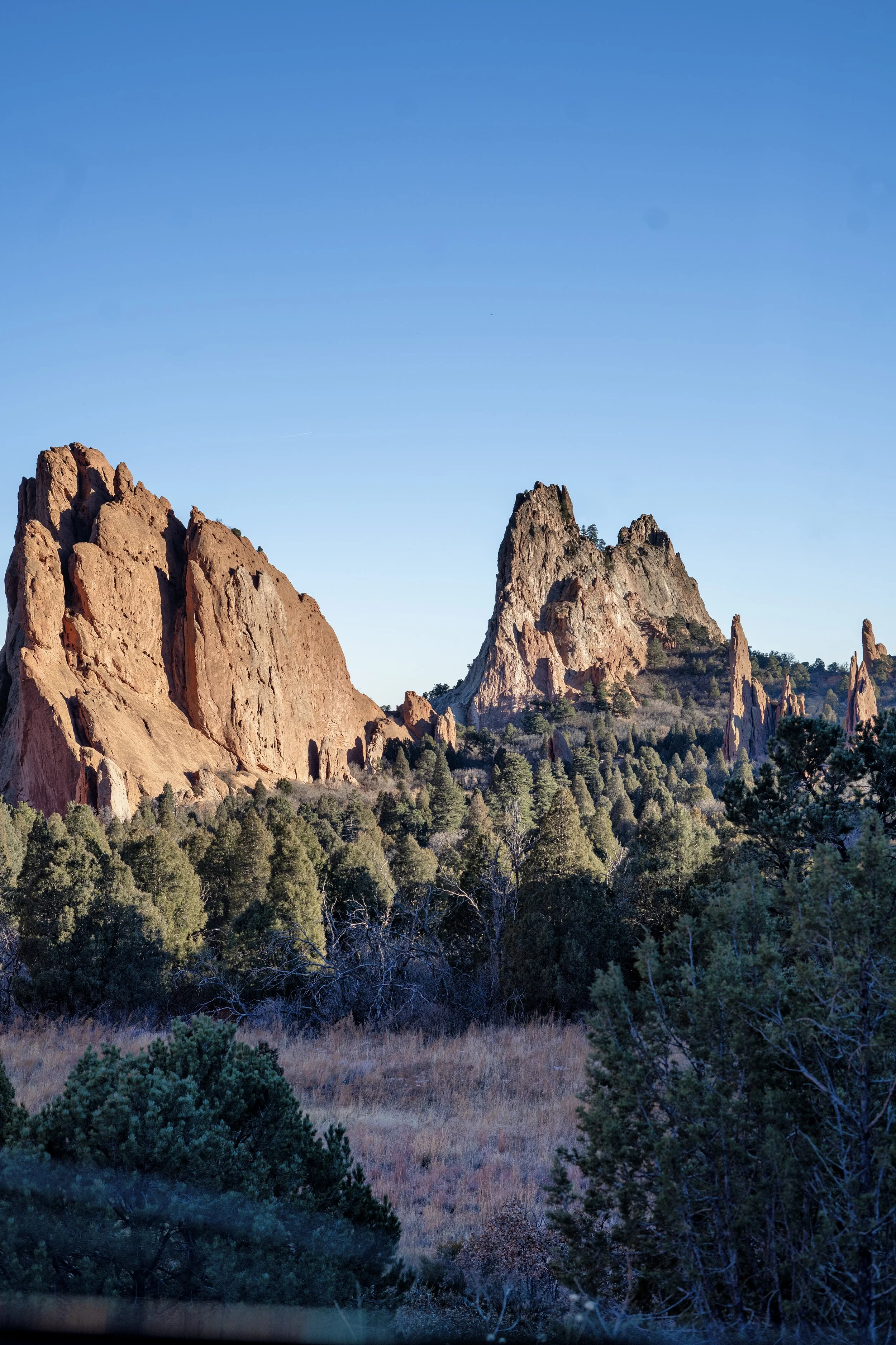 Rock formations and trees in a mountainous landscape under a clear blue sky.