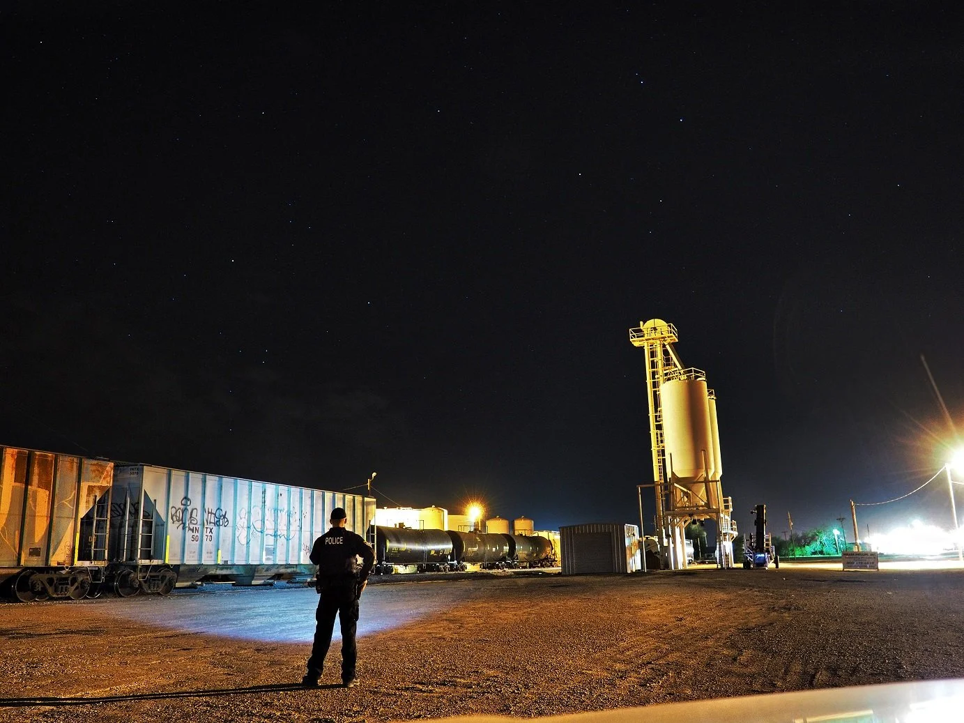 A Police Officer investigating a rail yard at a grainery in the late hours in rural West Texas circa 2018. 