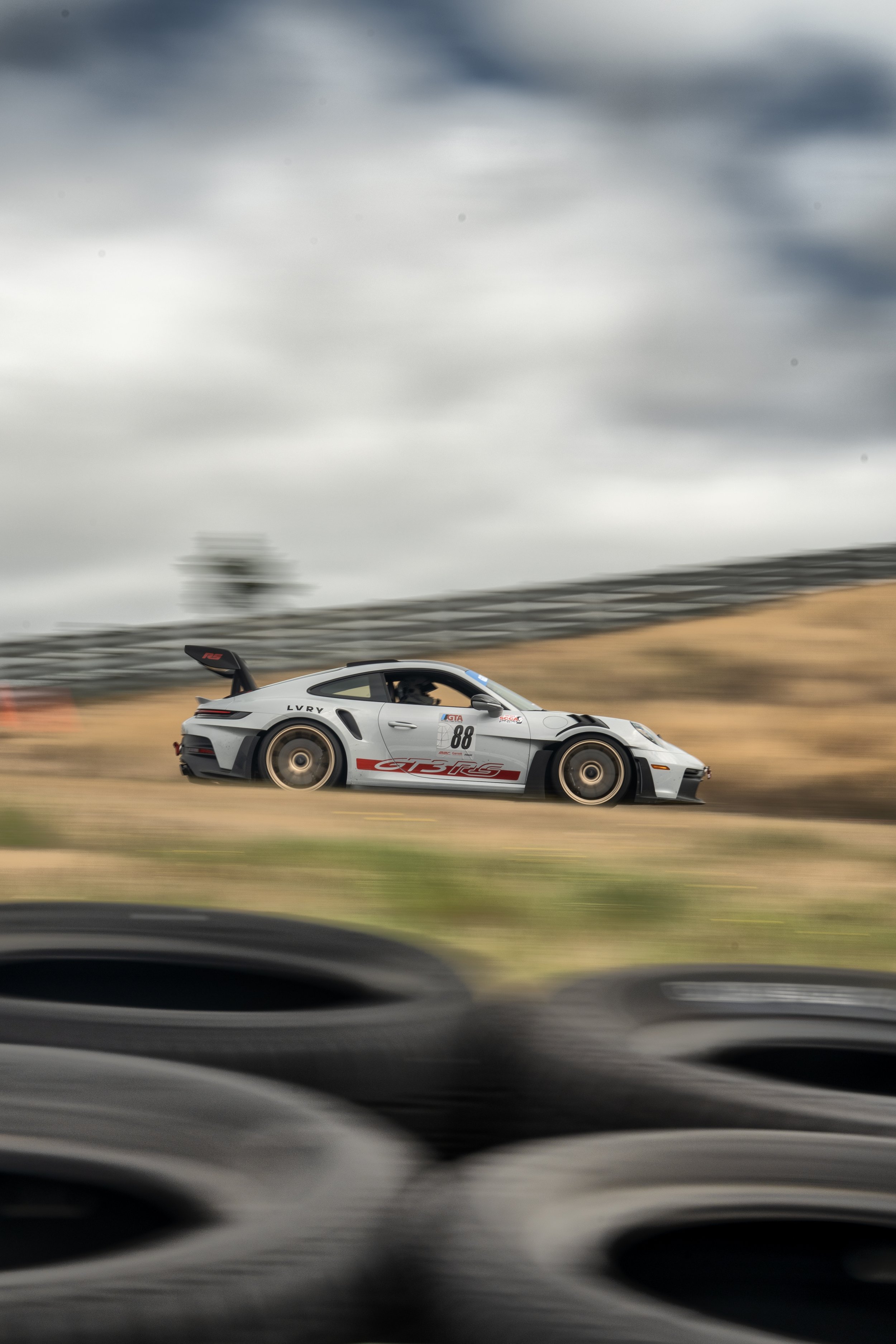 A white race car with the number 88 on its side racing on a track, with a blurred background indicating high speed.
