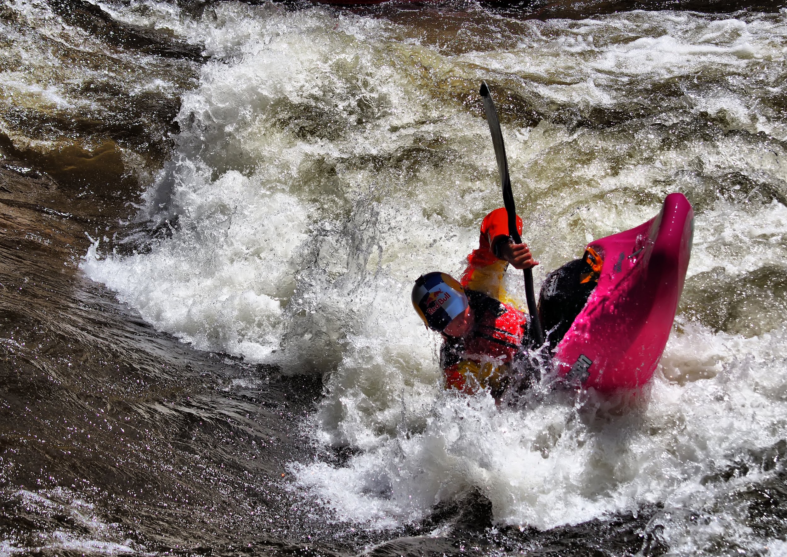 A person navigating white water rapids in a kayak, wearing a helmet and protective gear.