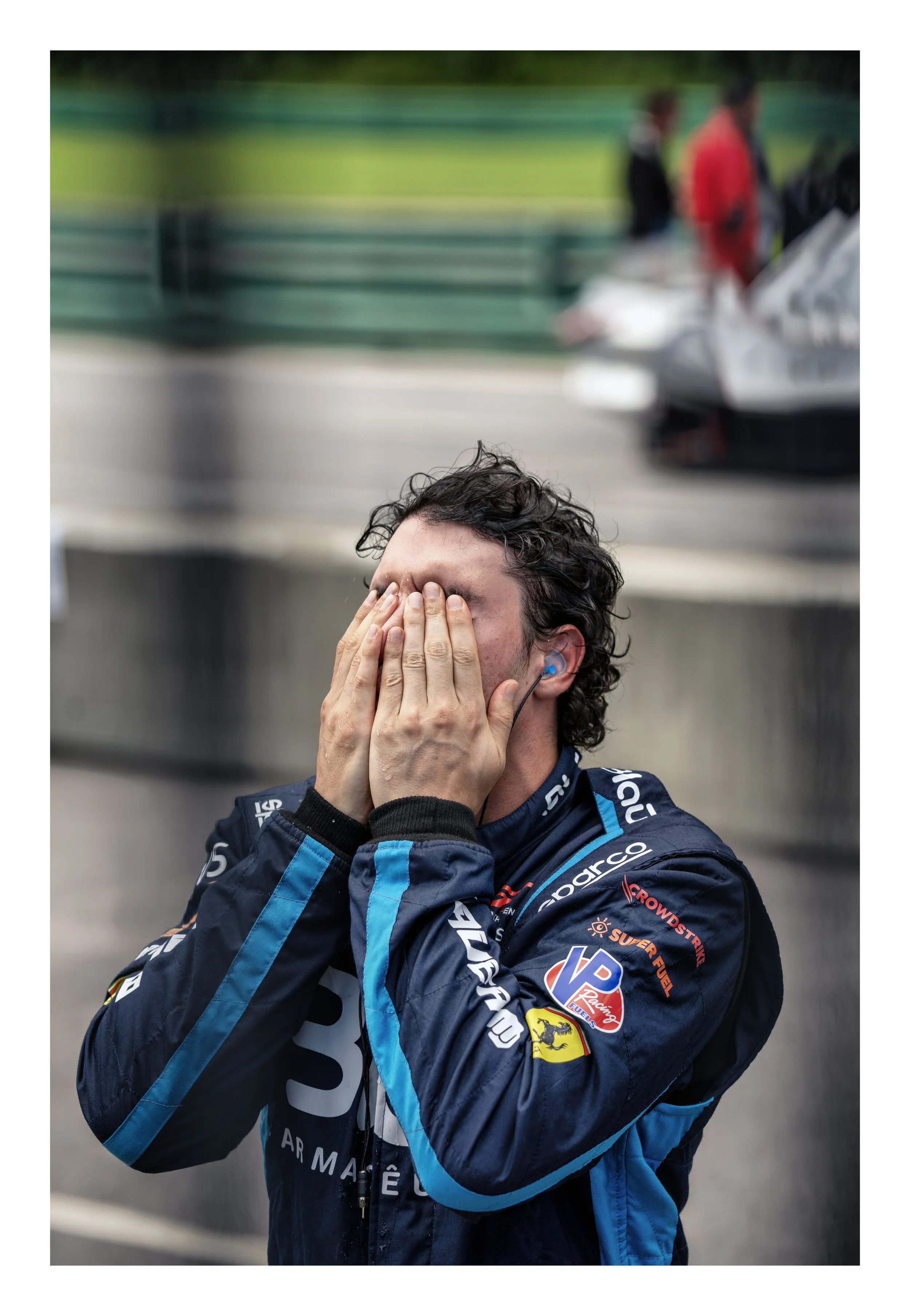 Race car driver in racing suit with hands covering face, emotional moment
