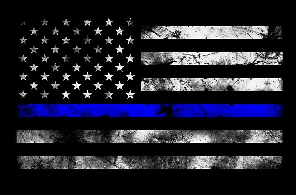 American flag with black and white stripes and a blue line in the middle, representing police support, on a dark background.