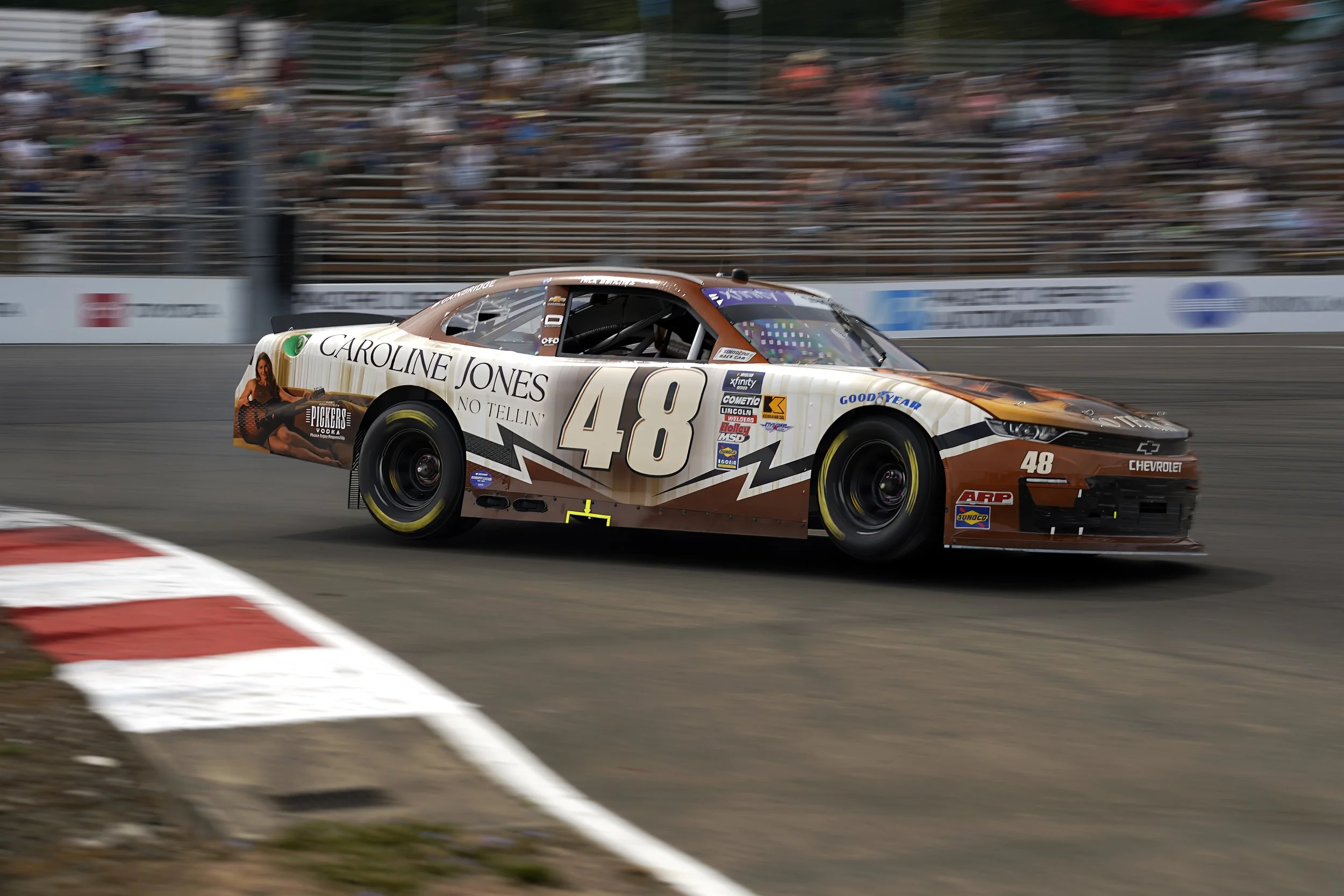 A race car with the number 48, sponsored by Chevrolet, is speeding on a racetrack with blurred spectators in the background.