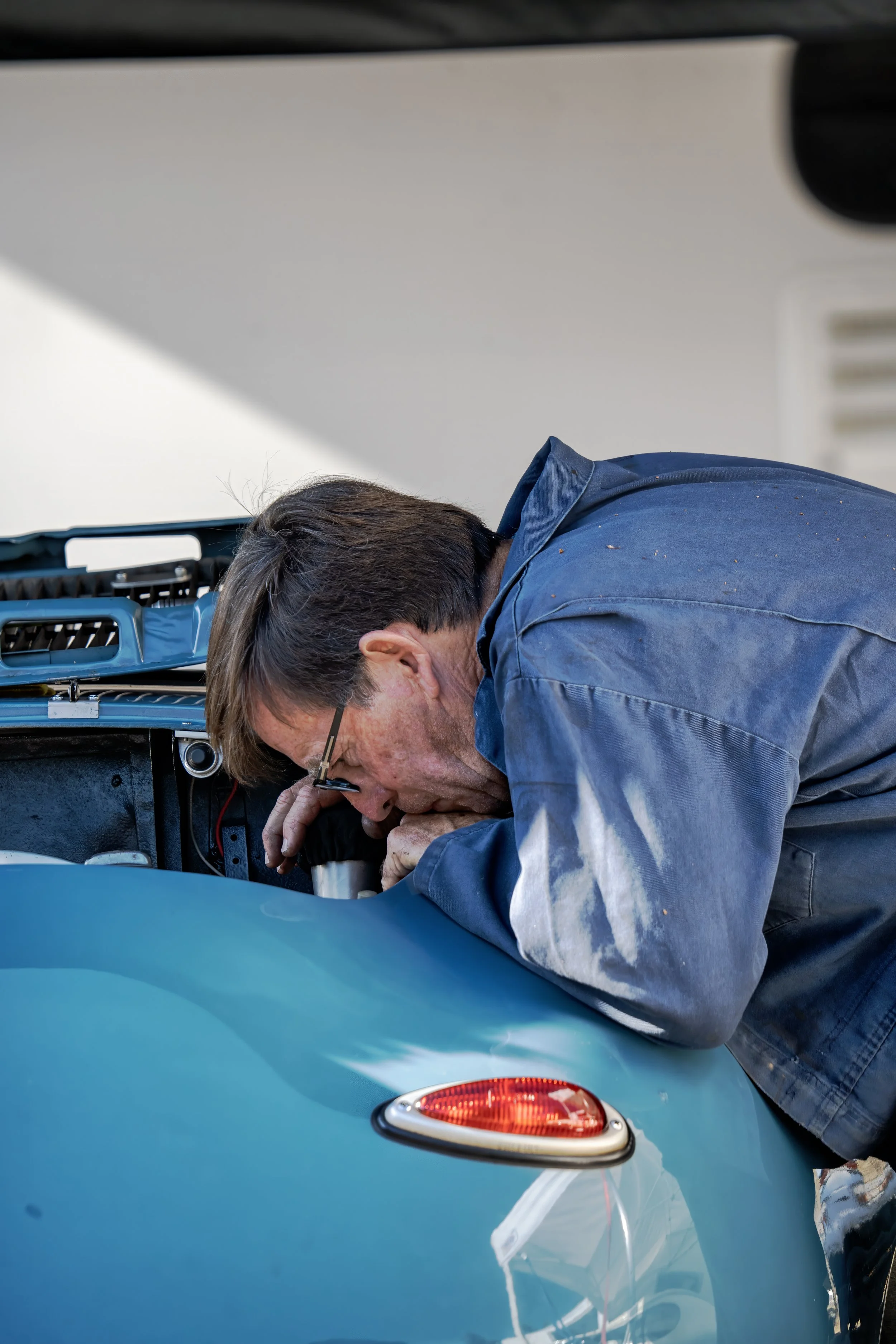 A man inspecting the engine of a blue car.