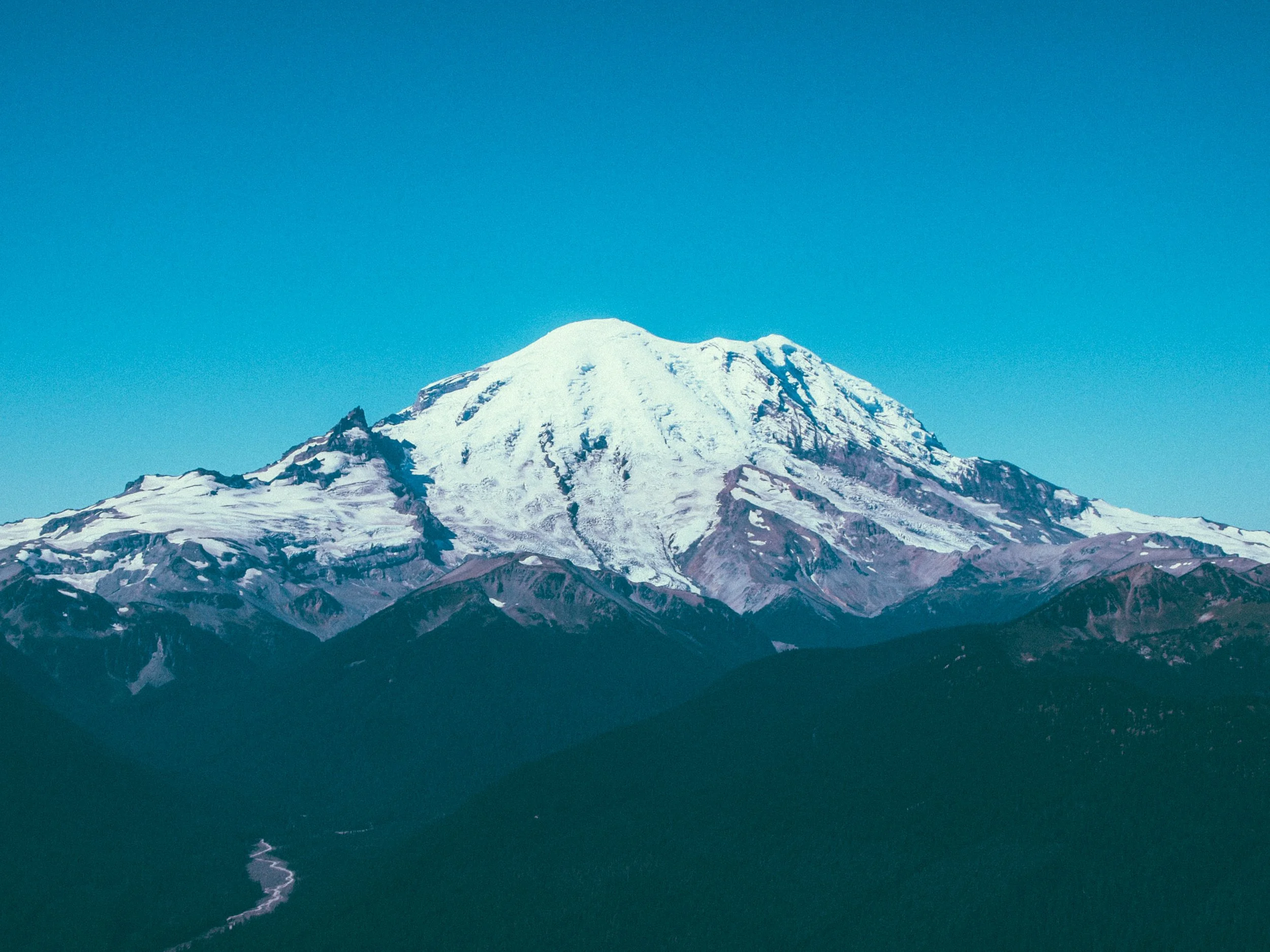 Snow-capped mountain with rocky slopes under a clear blue sky.