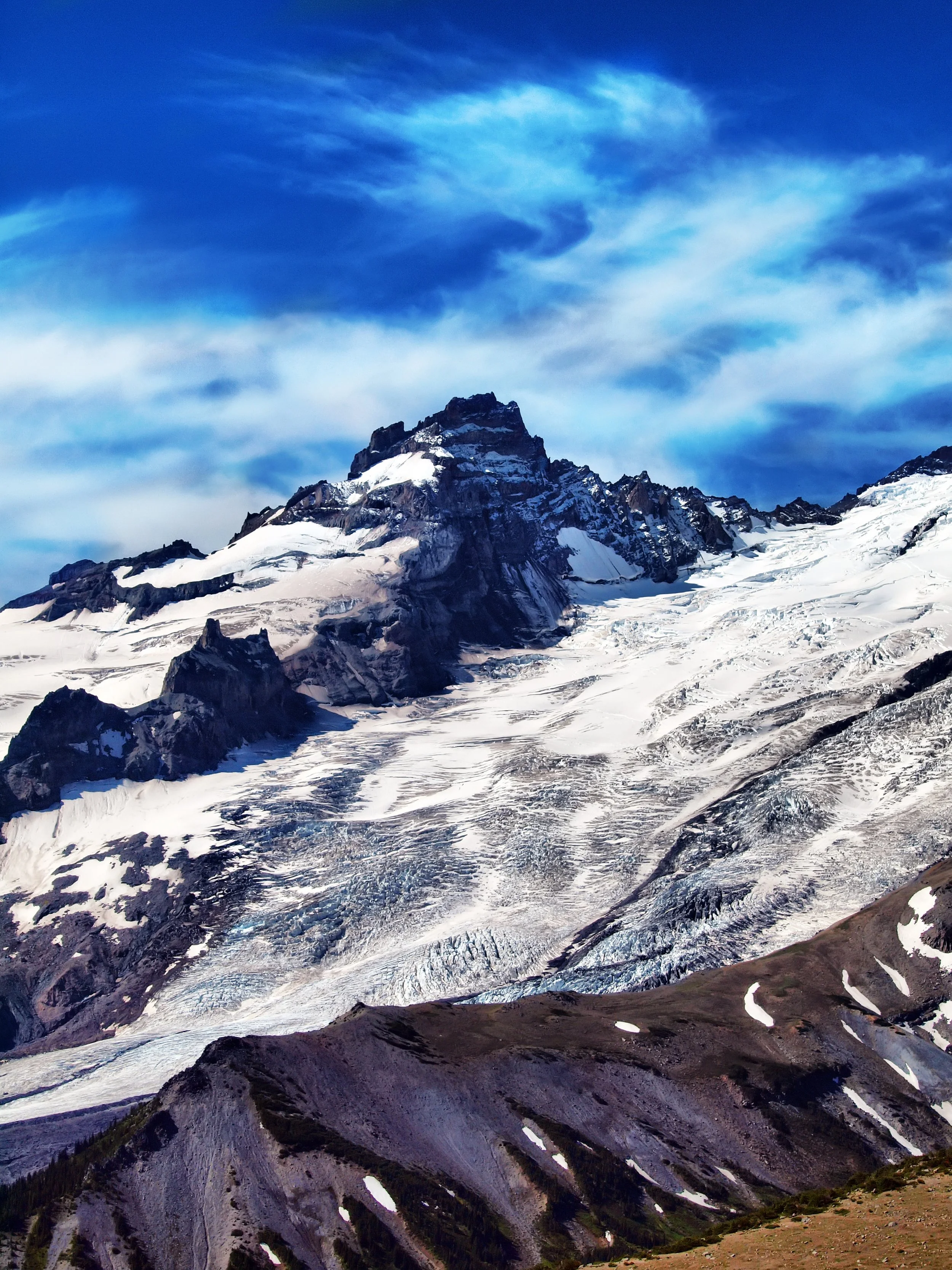 Snow-capped mountain peaks under a blue sky with wispy clouds.