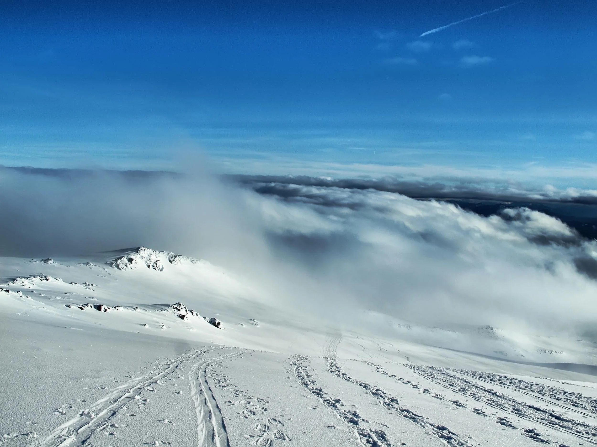 Snowy mountain landscape with ski tracks and clouds below the peaks.