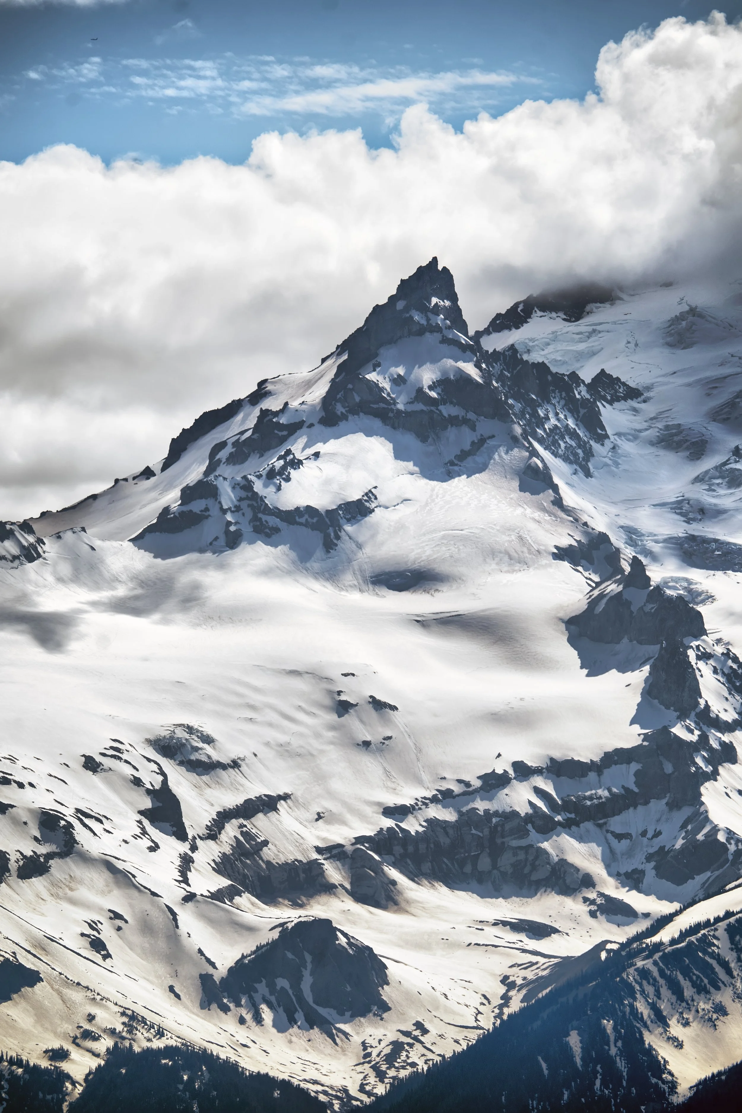 Snow-covered mountain range with sharp peaks, partly obscured by clouds, with a cloudy sky above.