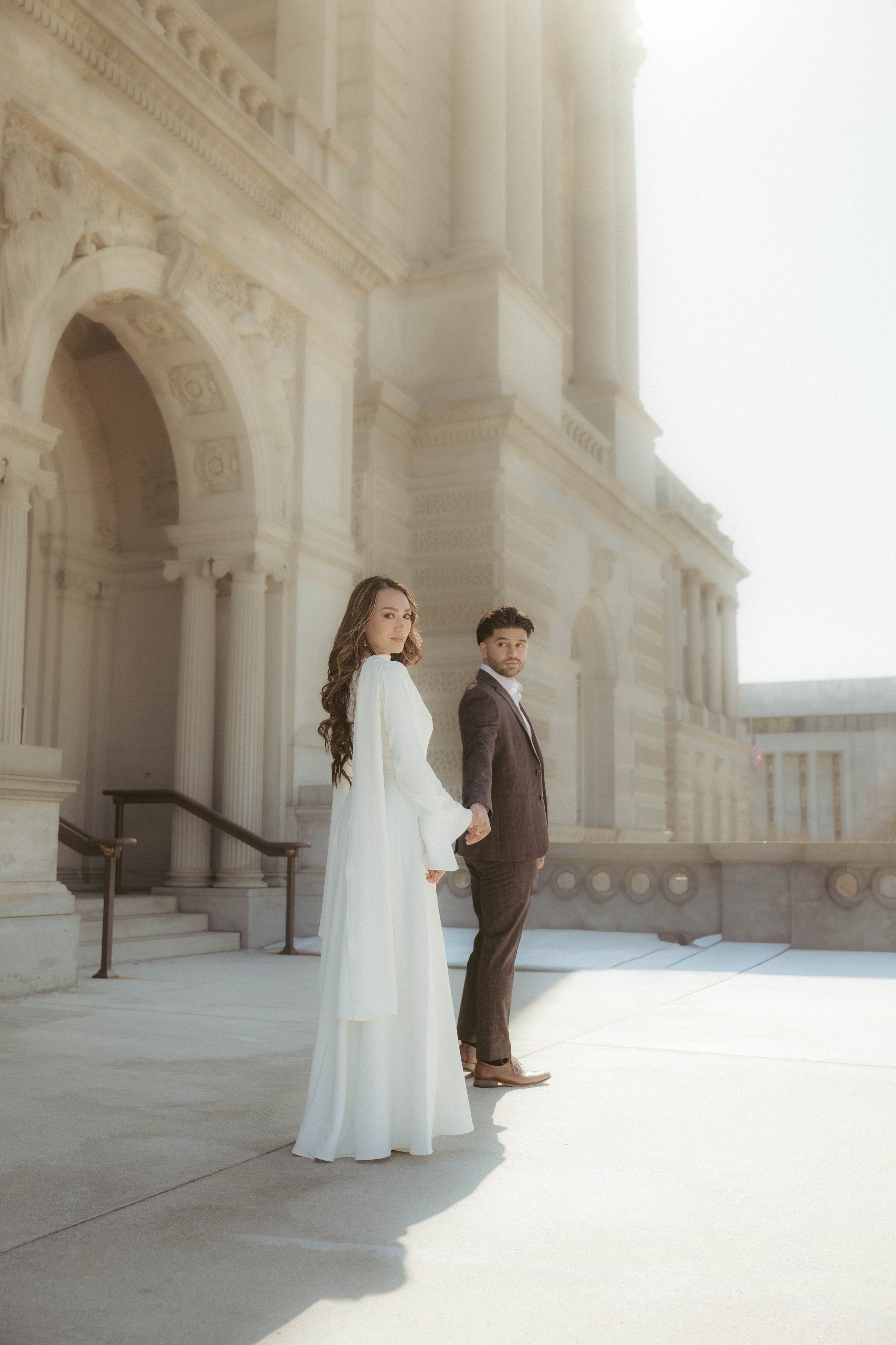 Warm, editorial portrait of a South Asian couple looking over their shoulder at the Library of Congress exterior; timeless engagement photography in Washington DC.