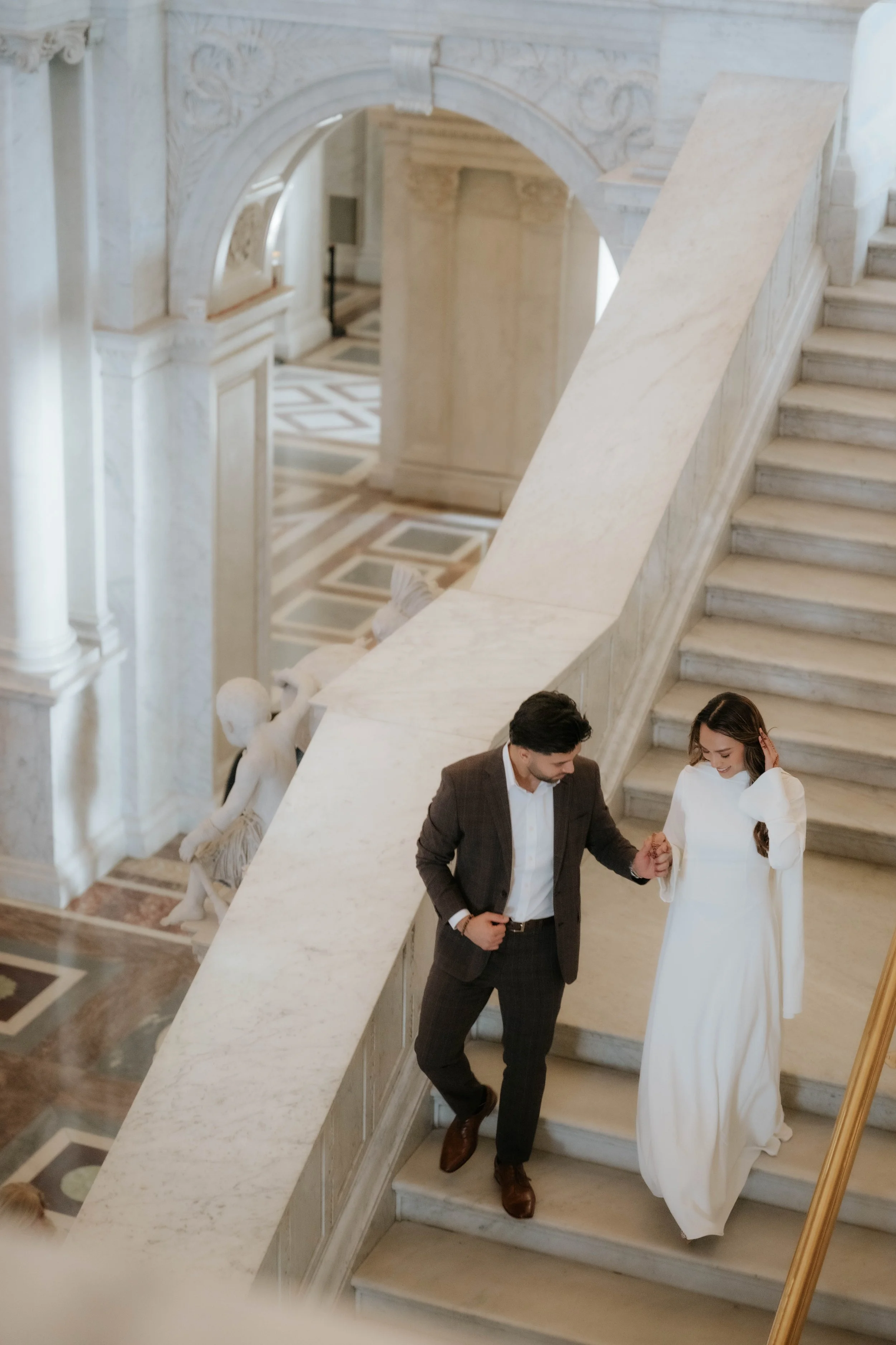 Couple holding hands walking down the staircase at the library of congress. Timeless, and editorial style and wardrobe. Award Winning Photographer - SNKWorks