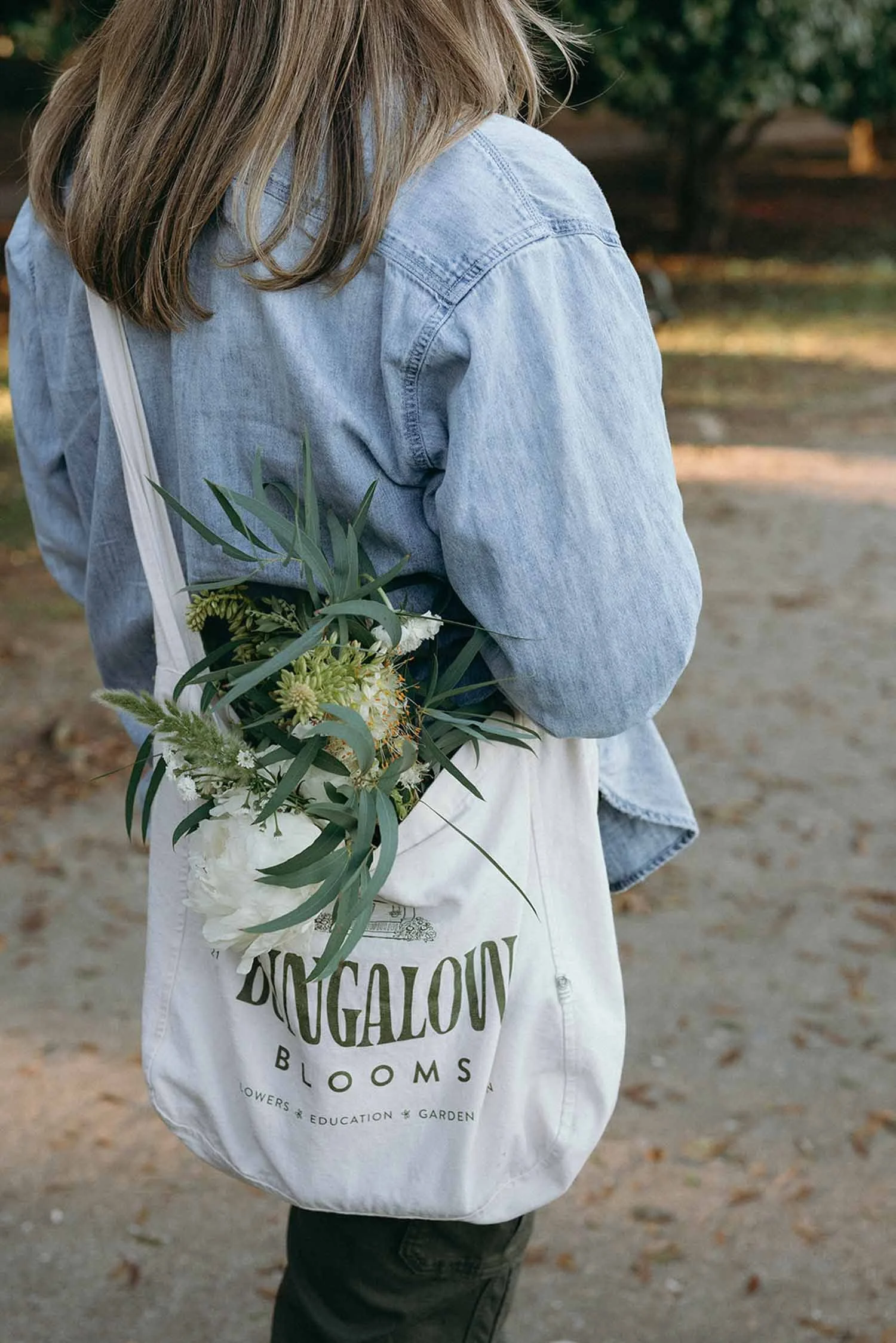 Alex walking away with a Bungalow Blooms tote bag over her shoulder and a whimsical flower bouquet peeking out.