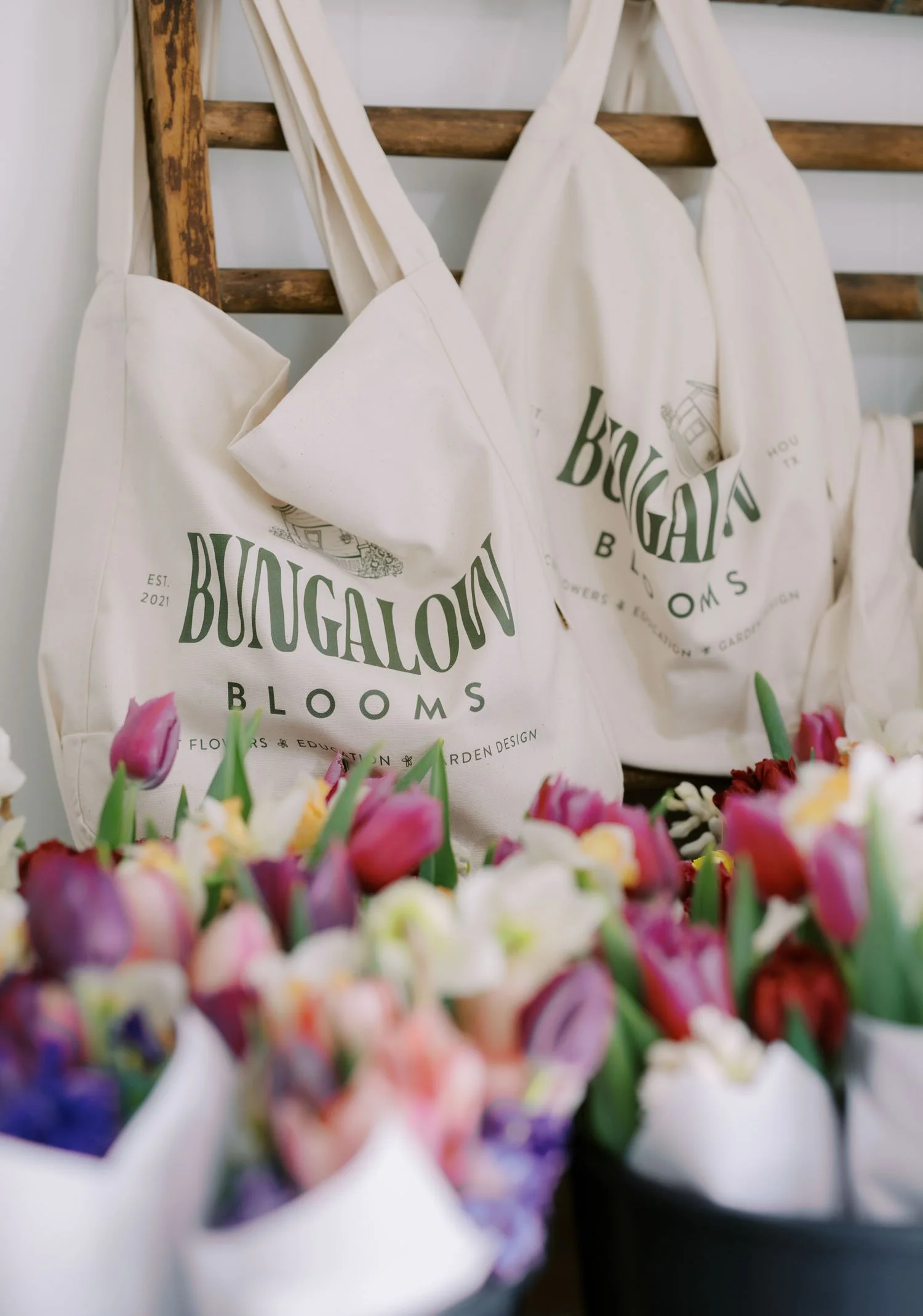 Bungalow Blooms tote bags hanging behind fresh tulip bouquets.
