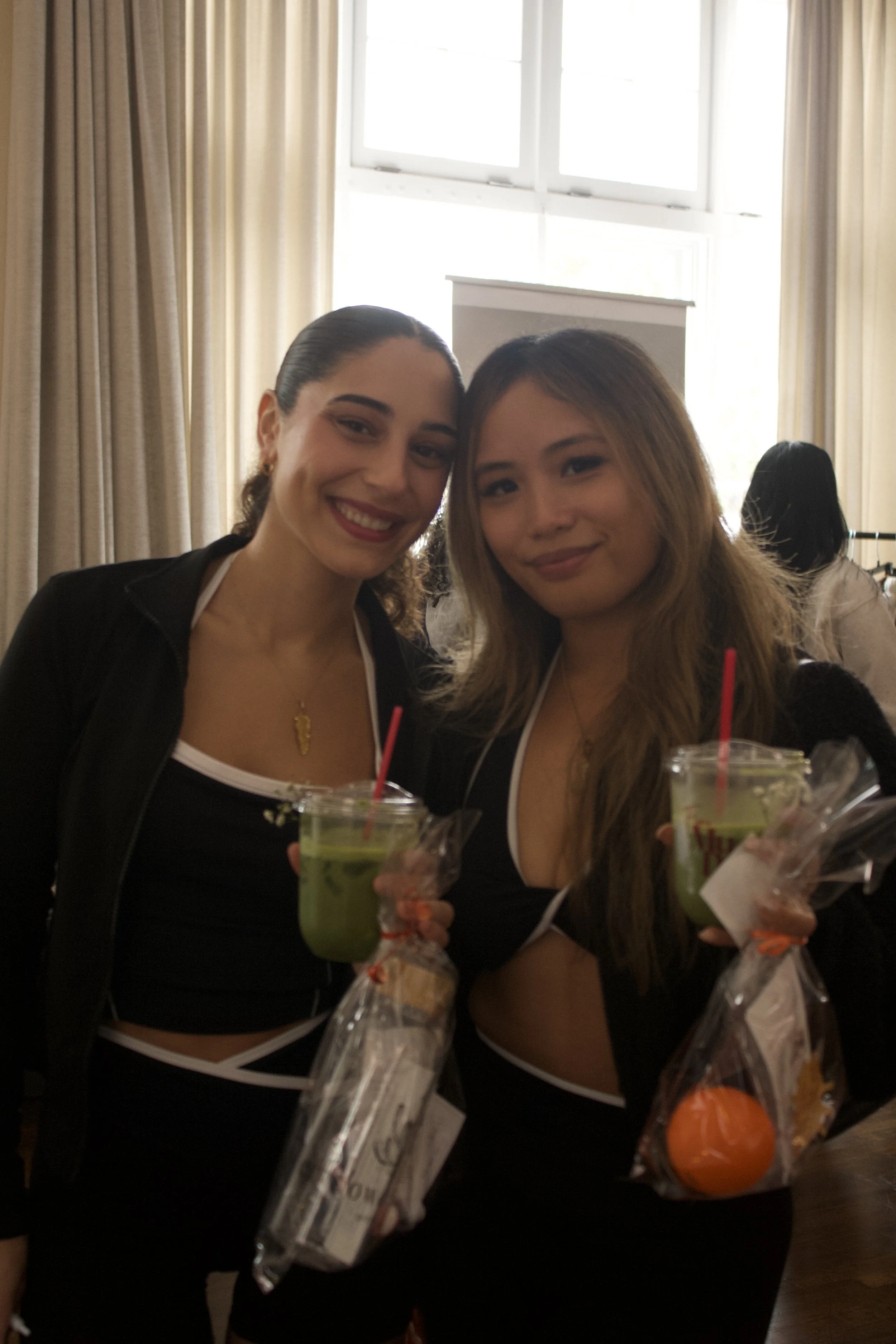 two women friends in black and white athletic wear, smiling with match and goody bag in hand