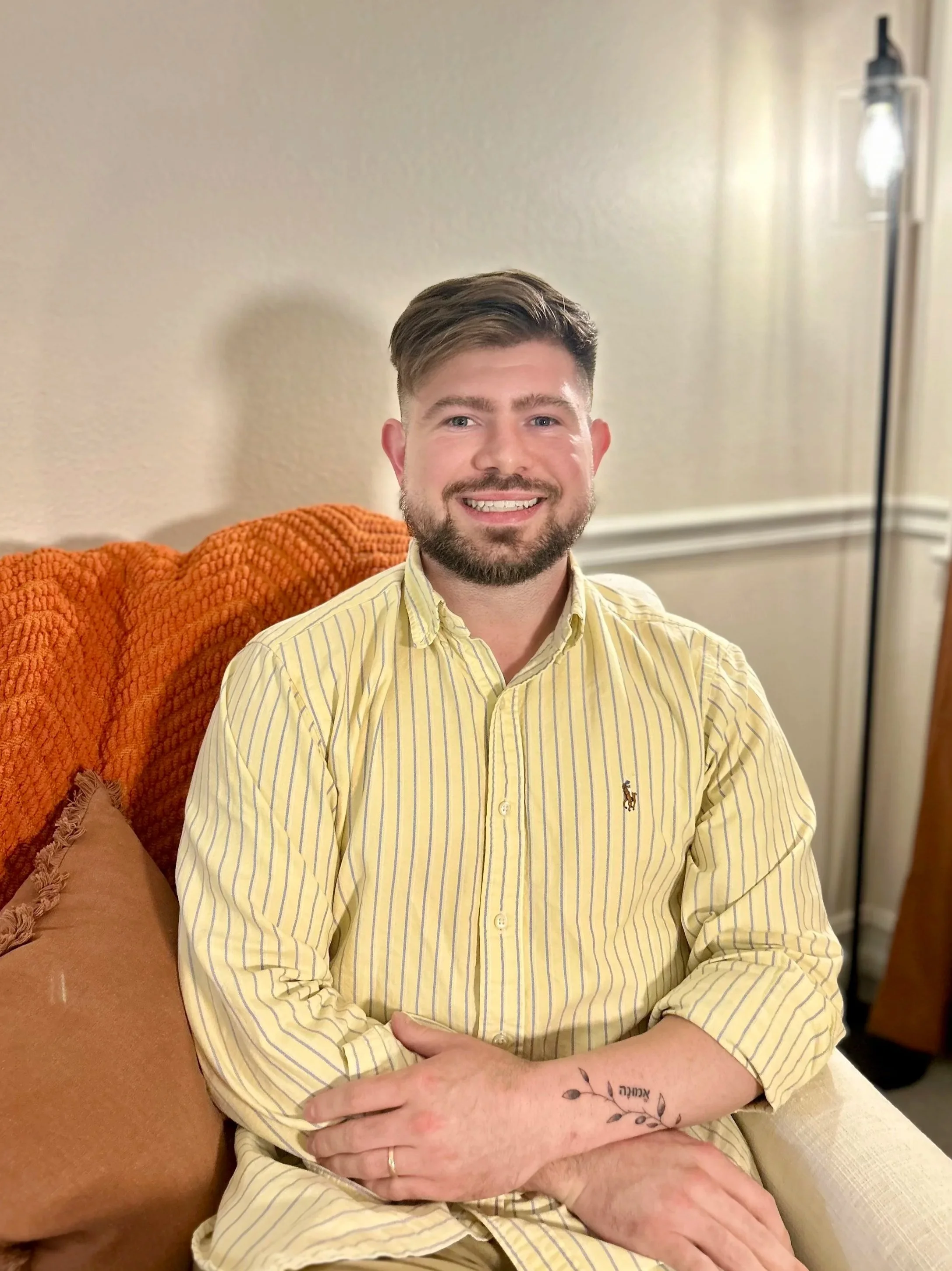 alan in a yellow and striped blue polo shirt, sitting down on in an beige office chair, smiling at the camera