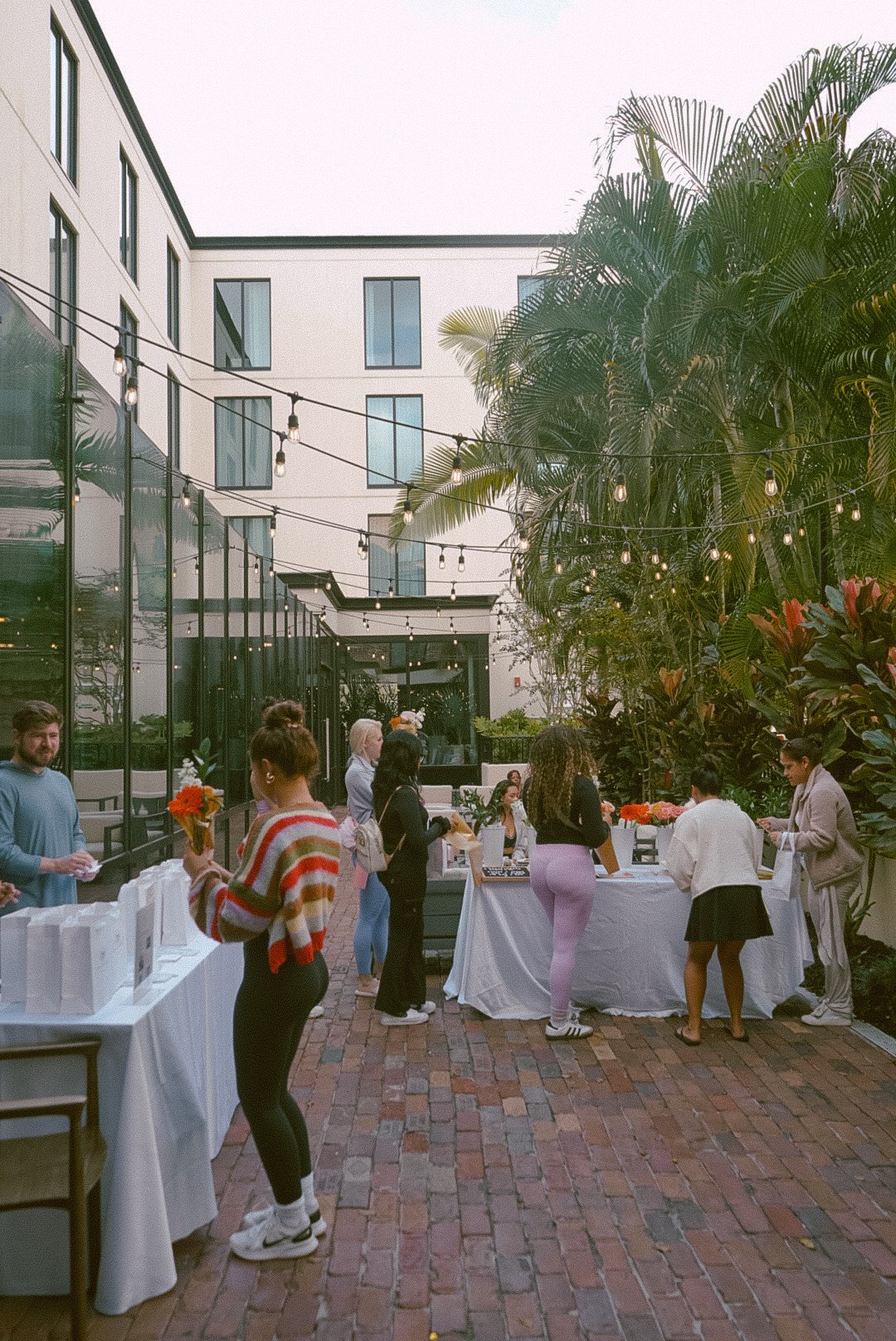 tabling in left quadrant and middle two quadrant of photo, with women in athletic wear at each table, and holding flowers in hand, at the courtyard of a hotel