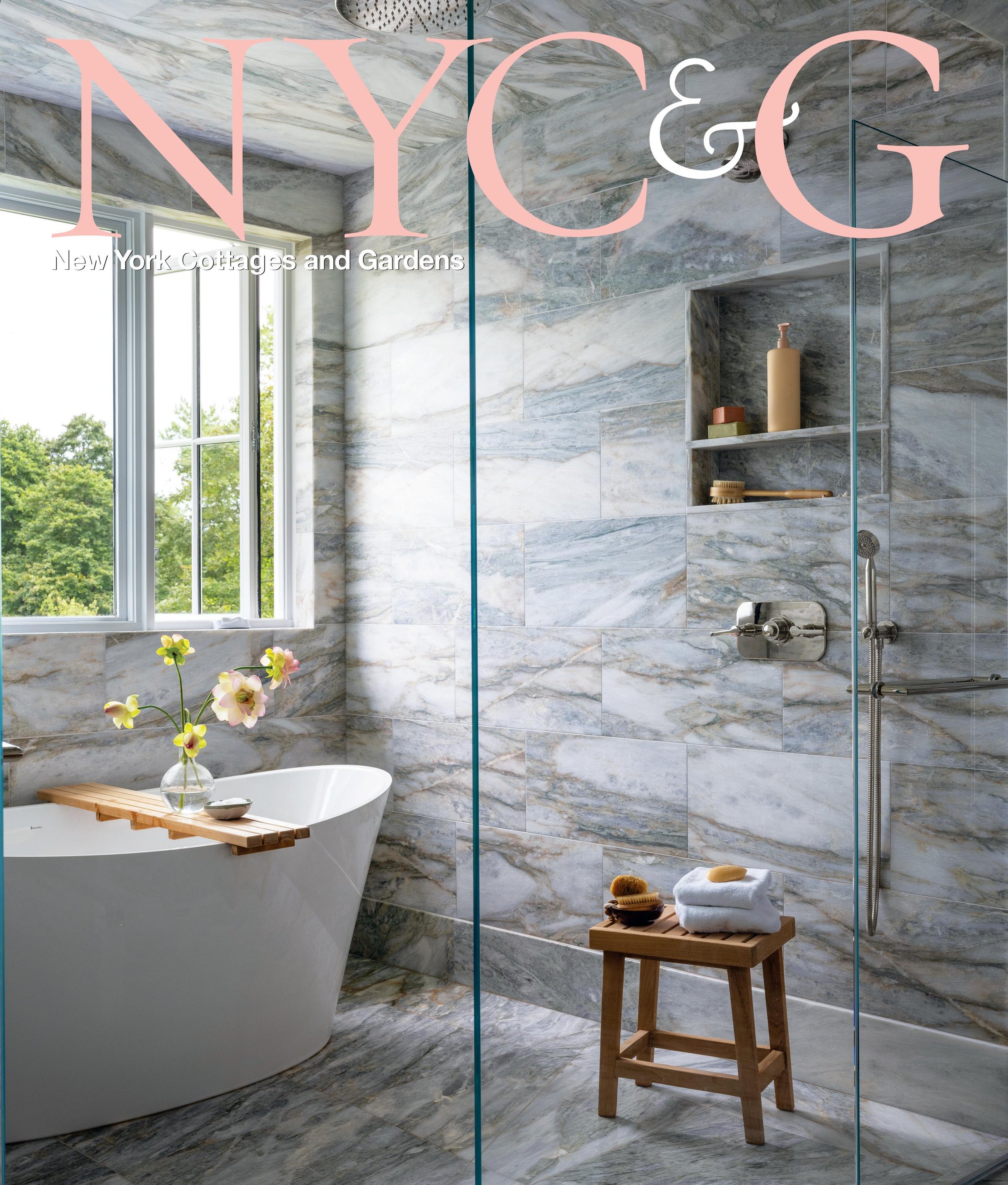 Modern bathroom with a freestanding bathtub, marble walls and floors, a window with a view of trees, and a wooden stool with towels and bath accessories.