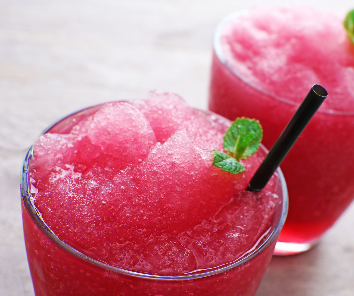 Bright pink frozen drink with black straw and green mint leaves.  Refreshing summer wine drink.