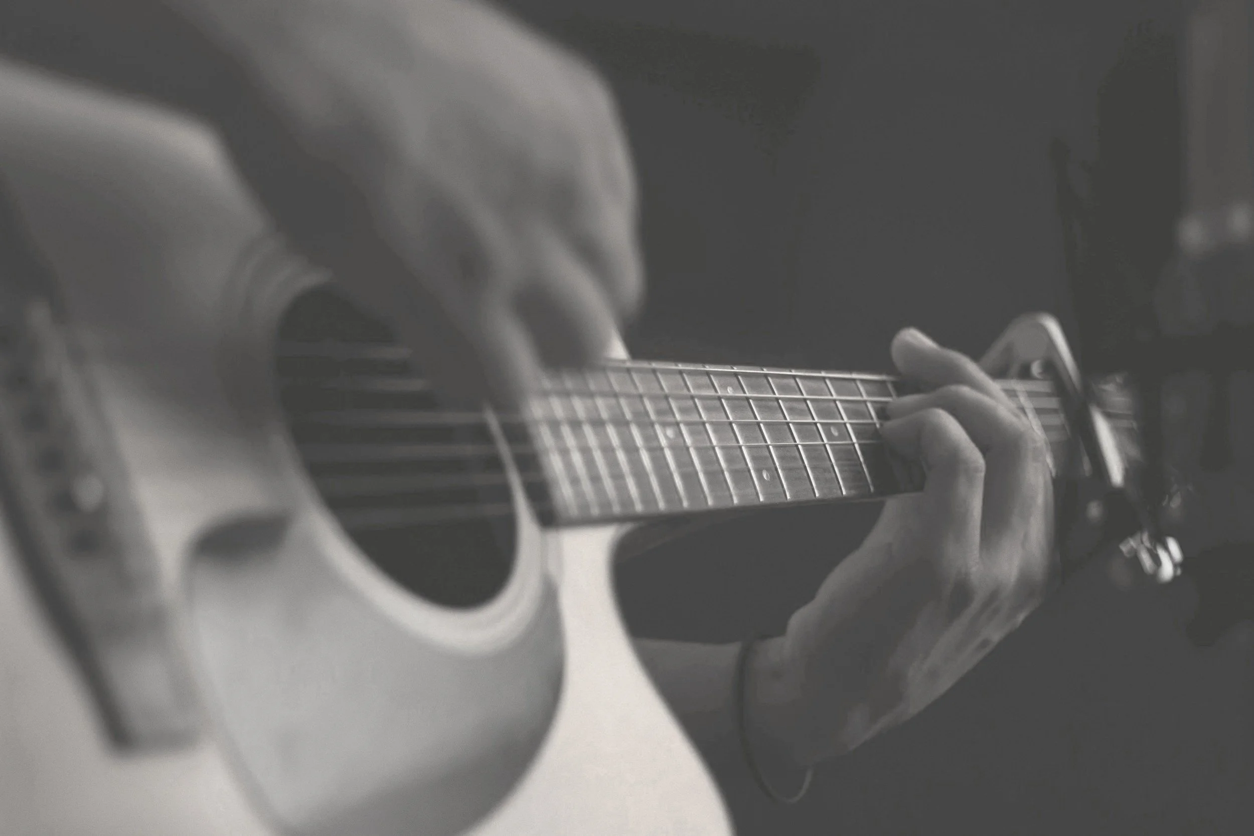 A person playing an acoustic guitar, with their fingers on the fretboard, in black and white.