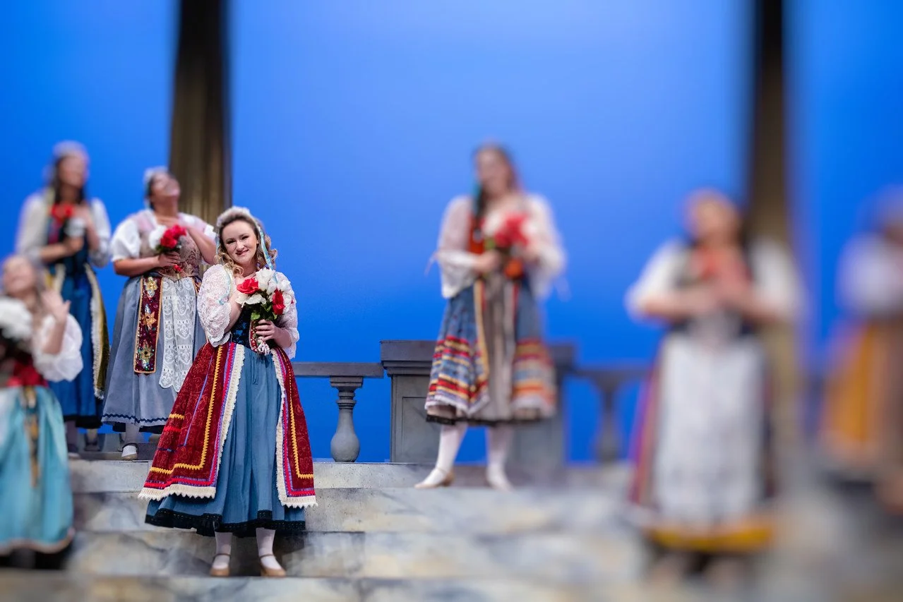 Women in traditional European costumes with floral bouquets on stage in a play or performance