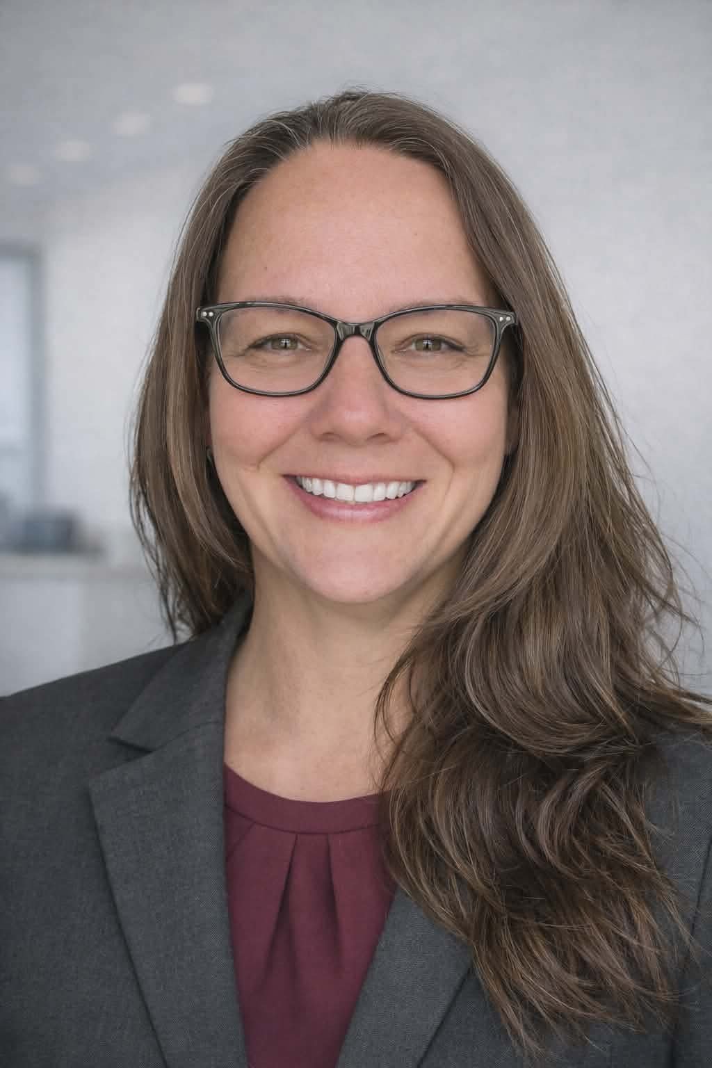 A smiling woman with long brown hair standing in front of a white wall with the word 'PROSPERITY' and the year '2024' on it, decorated with string lights and branch-like decor.