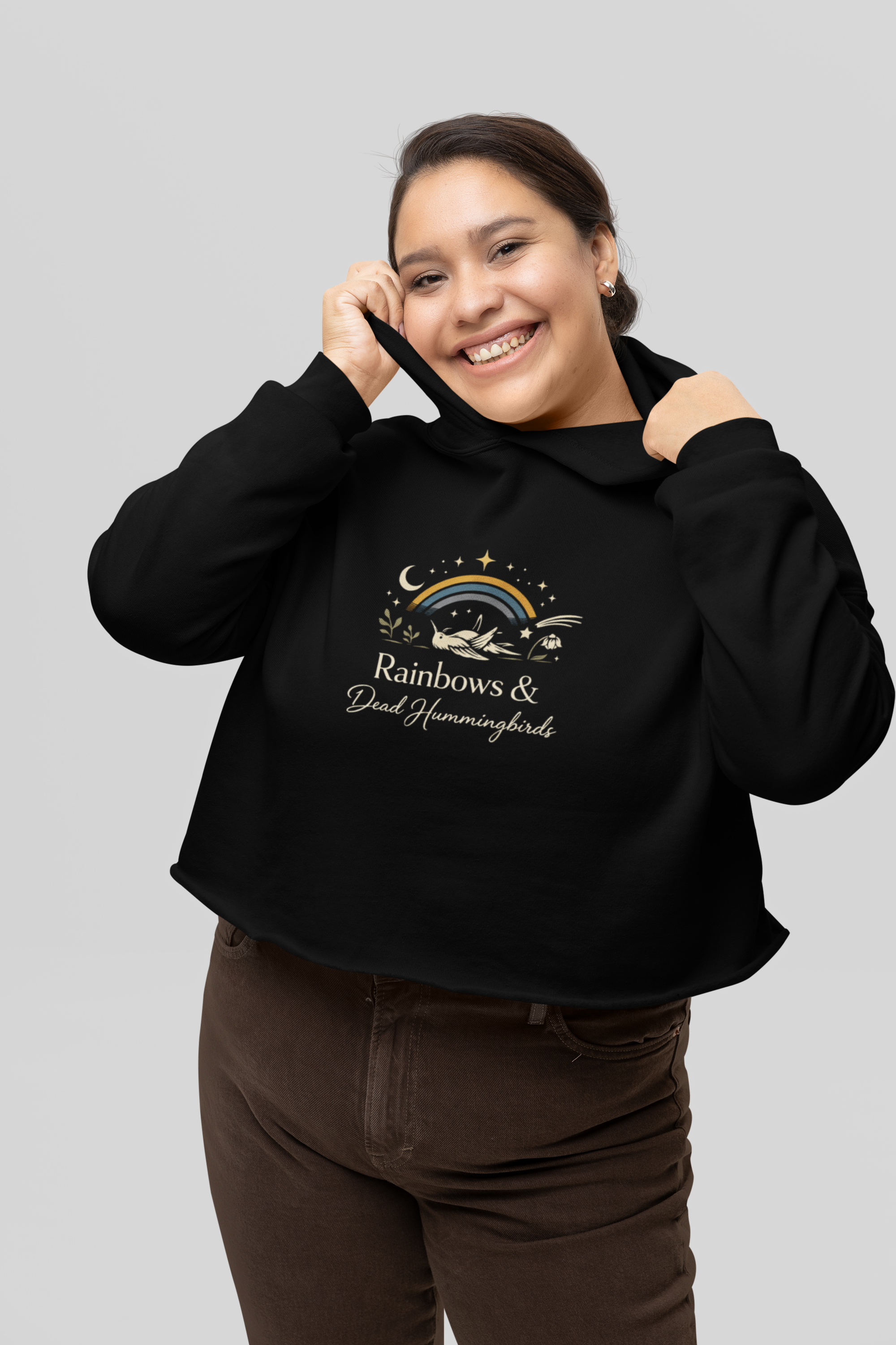 Woman wearing black Rainbows and Dead Hummingbirds sweatshirt in a cozy, neutral setting