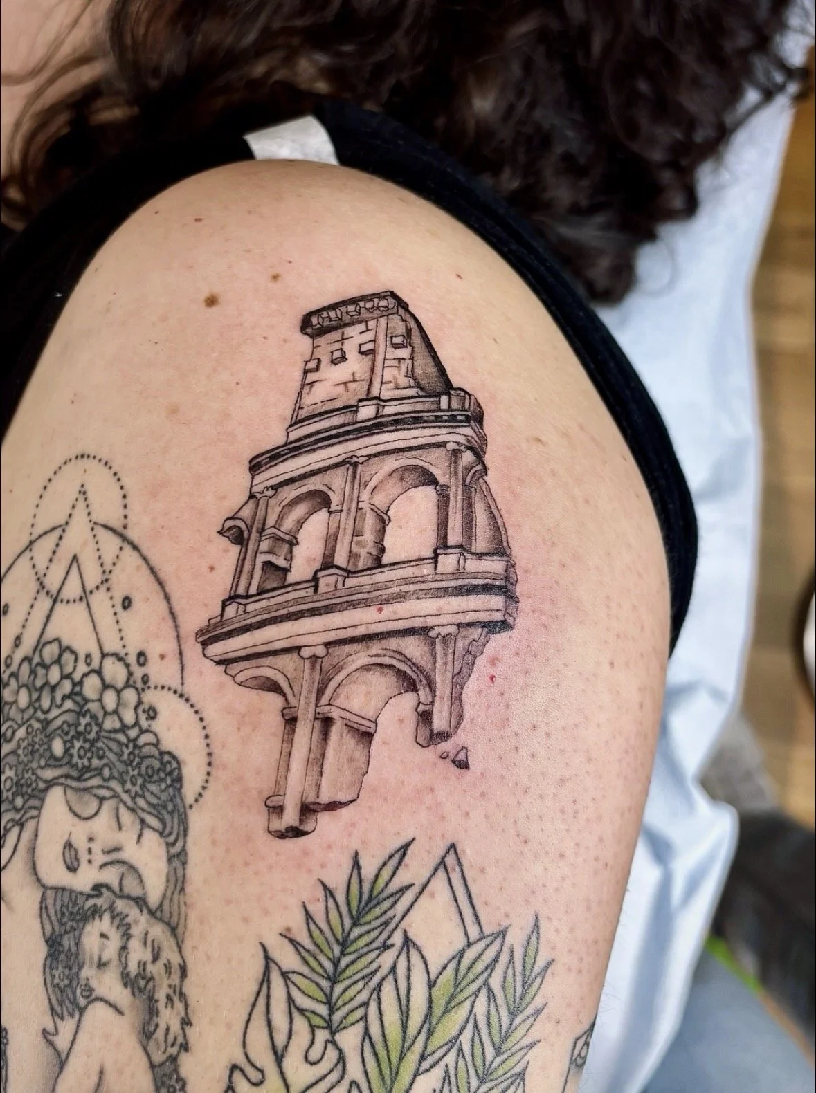 Tattoo of a detailed architectural structure resembling a the roman colosseum on a person's upper arm.