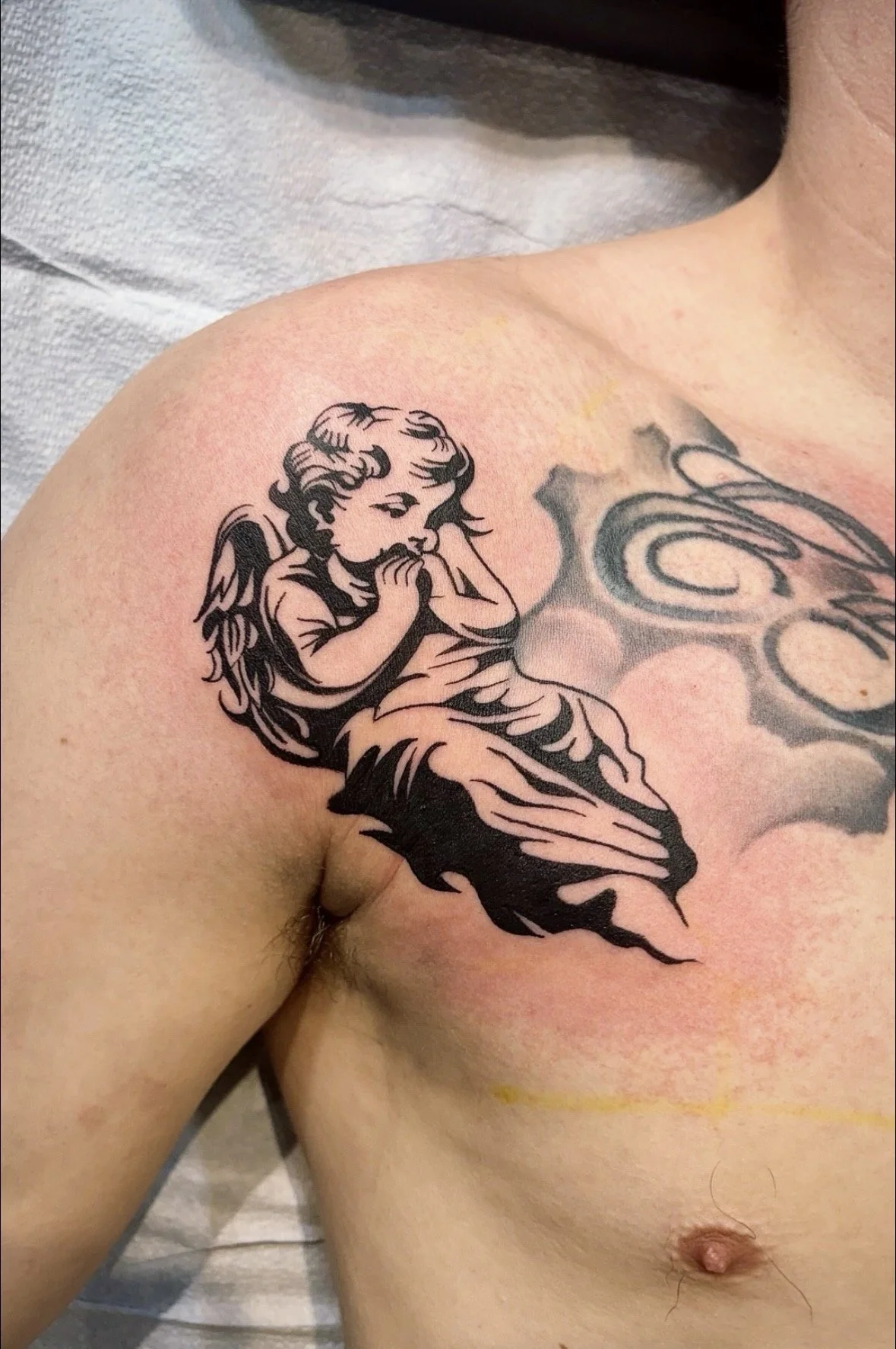 Tattoo of a young girl sitting with head bowed and hands clasped, located on the person's shoulder and upper chest.