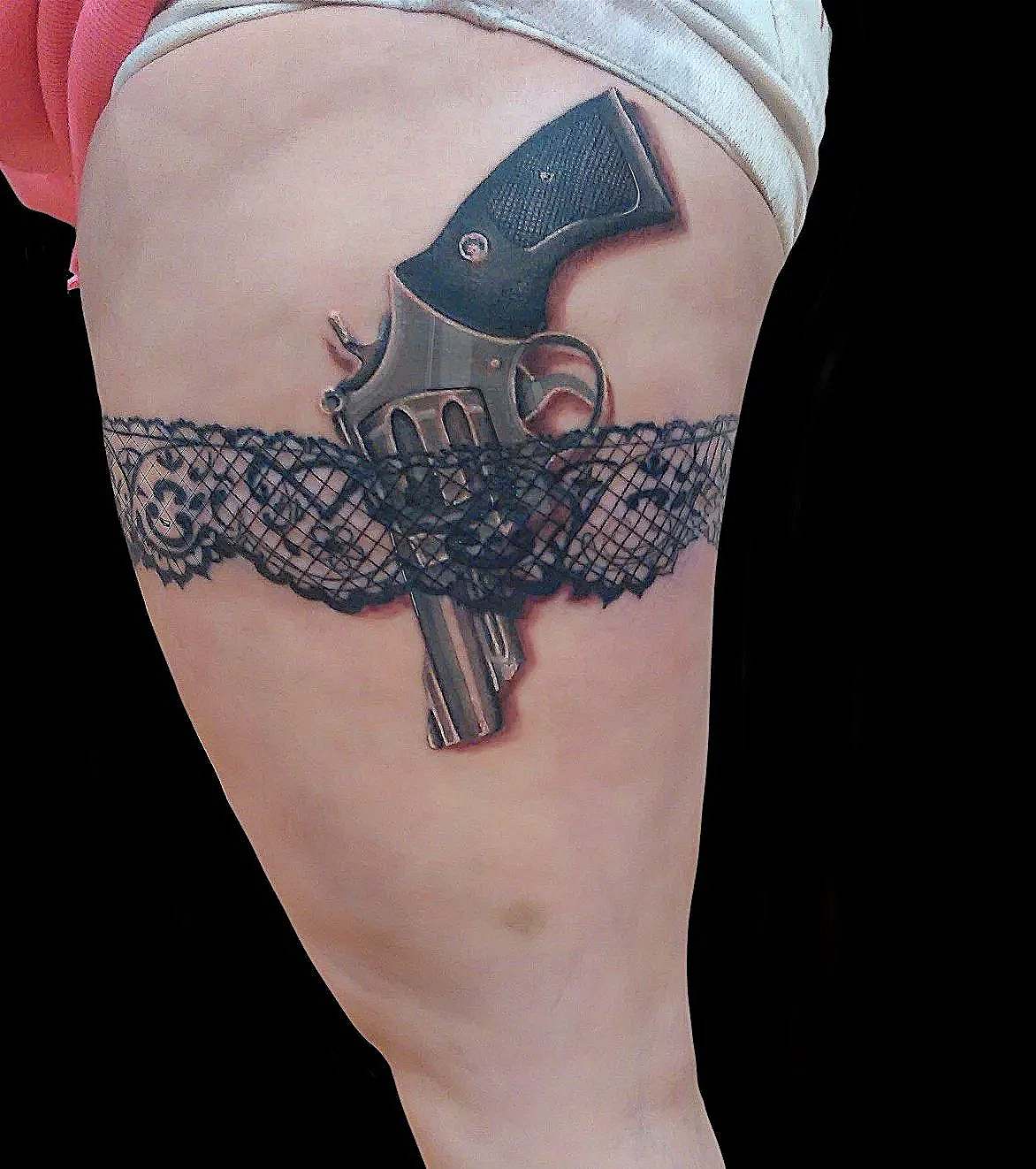 Tattoo of a revolver gun with a fishnet pattern and a banner with text on a person's upper thigh.